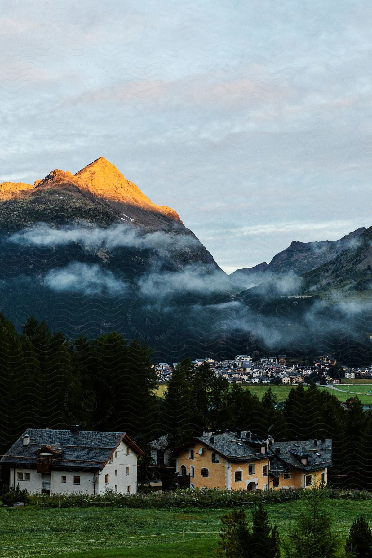 A region with a village of large houses next to forests and high mountains with fog on top