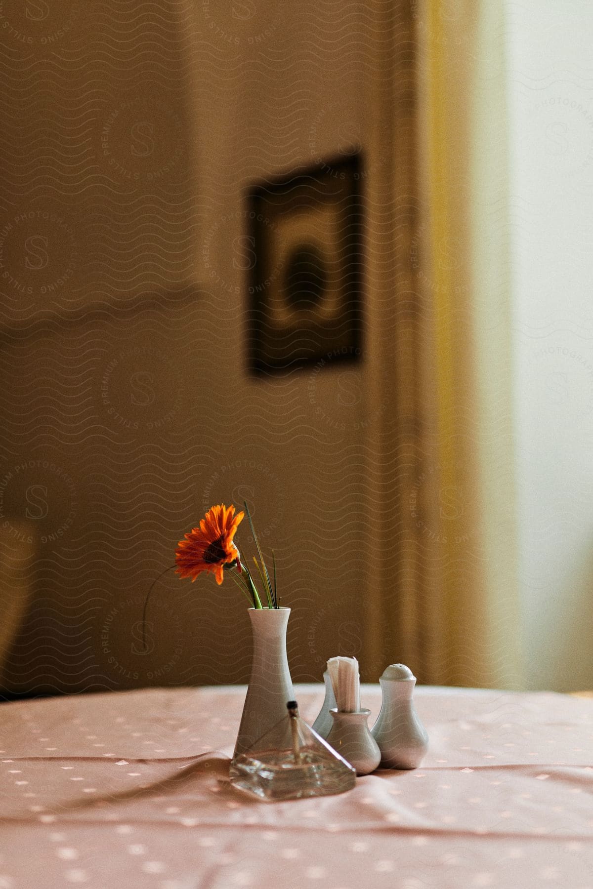 A table with a pink cloth and some decorations on top and a small vase with an orange flower