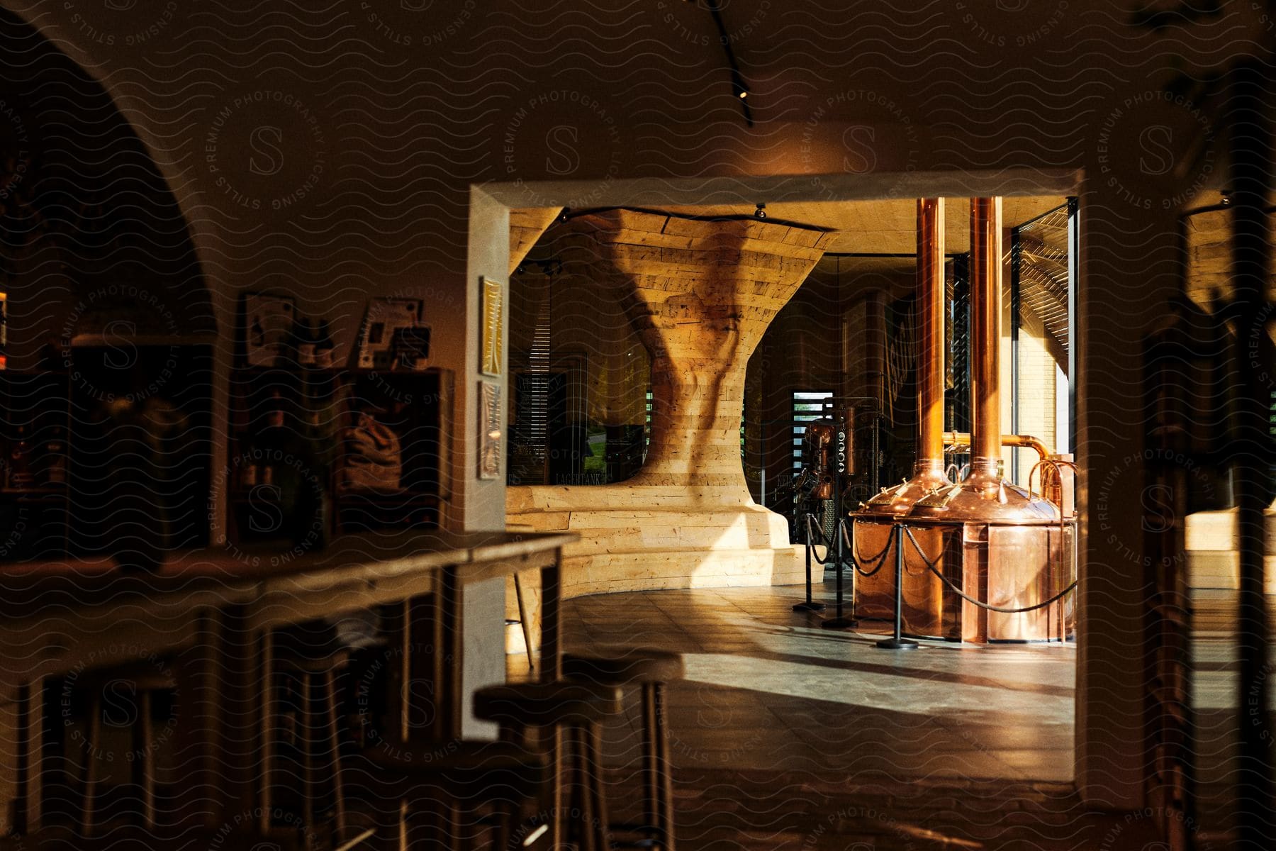 View into a distillery with copper kettles through an arched doorway from a bar area.