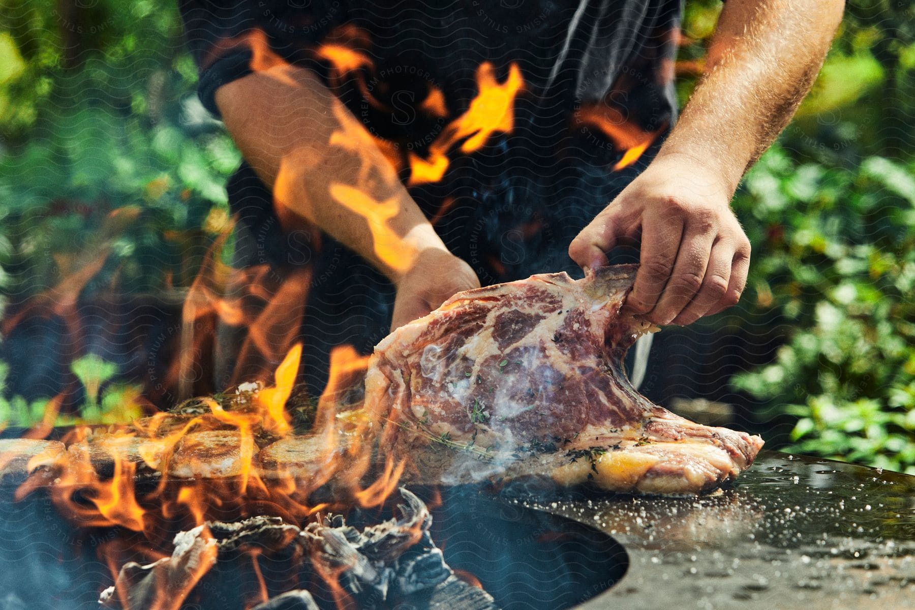 A man cooks a large piece of meat outdoors during the summertime.