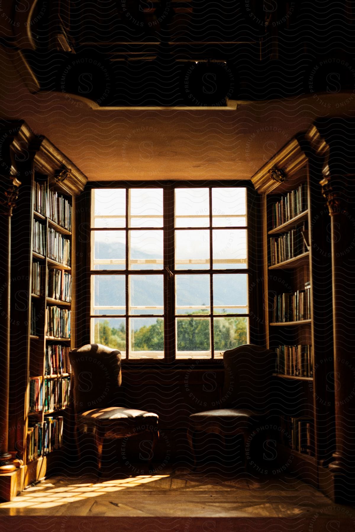 Cozy reading nook with water views, flanked by bookshelves and two chairs by a large window.