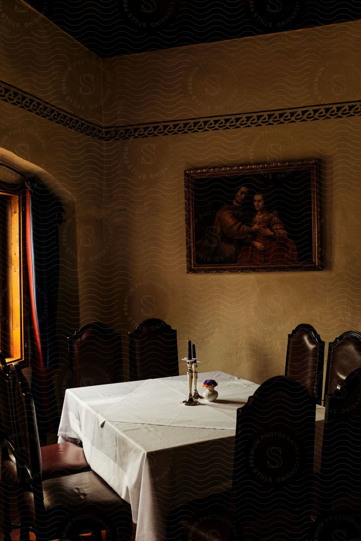 A dining table still not set, decorated with cloth and candles, and surrounded by antique chairs