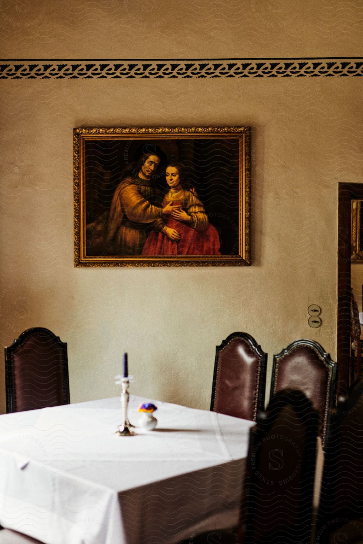 The interior of a room where there is a table with some chairs and on the wall there is an old painting