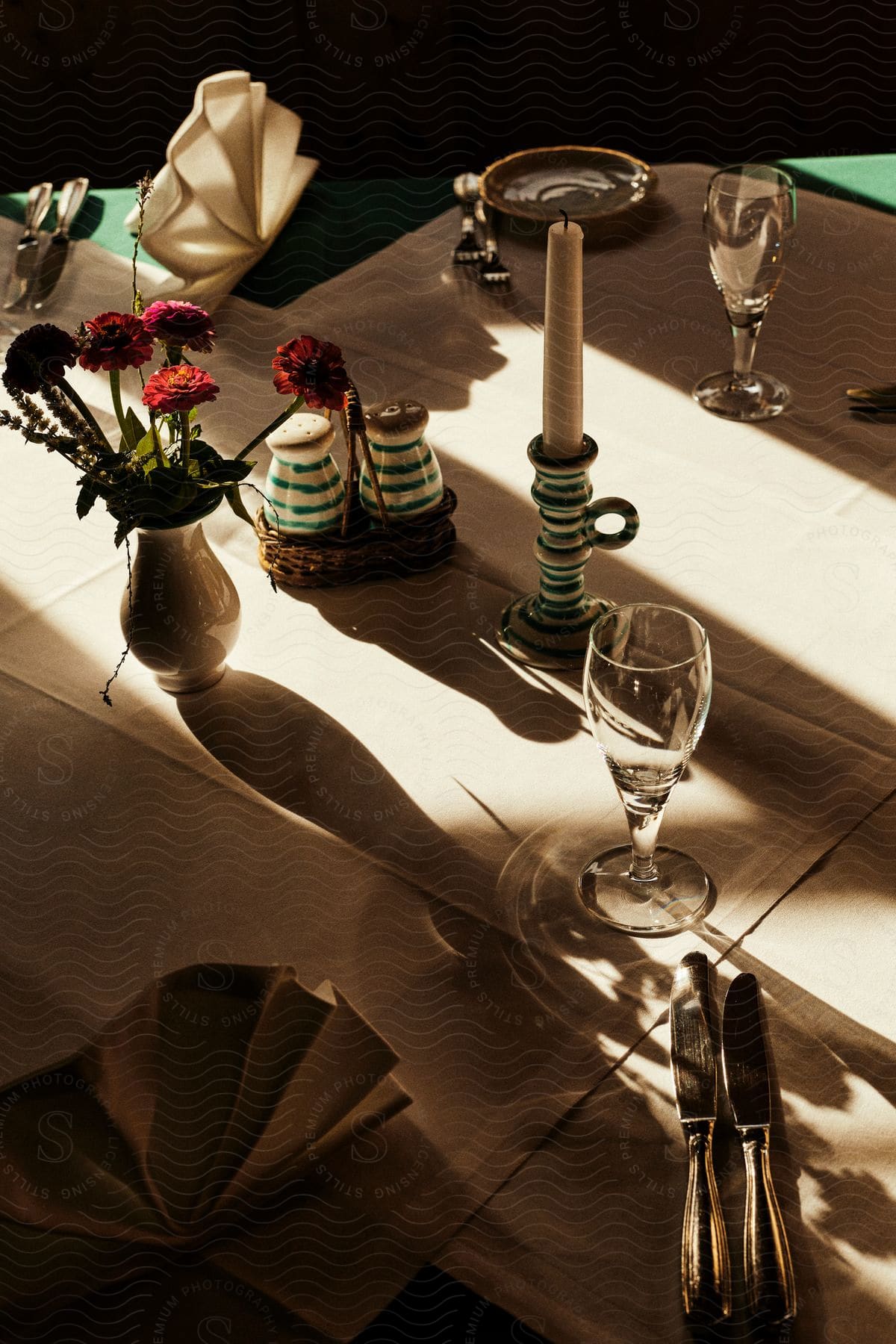 A simple and elegant tablesetting features a white tablecloth, a lit candle in a glass hurricane, and a colorful bouquet of flowers in a clear vase.