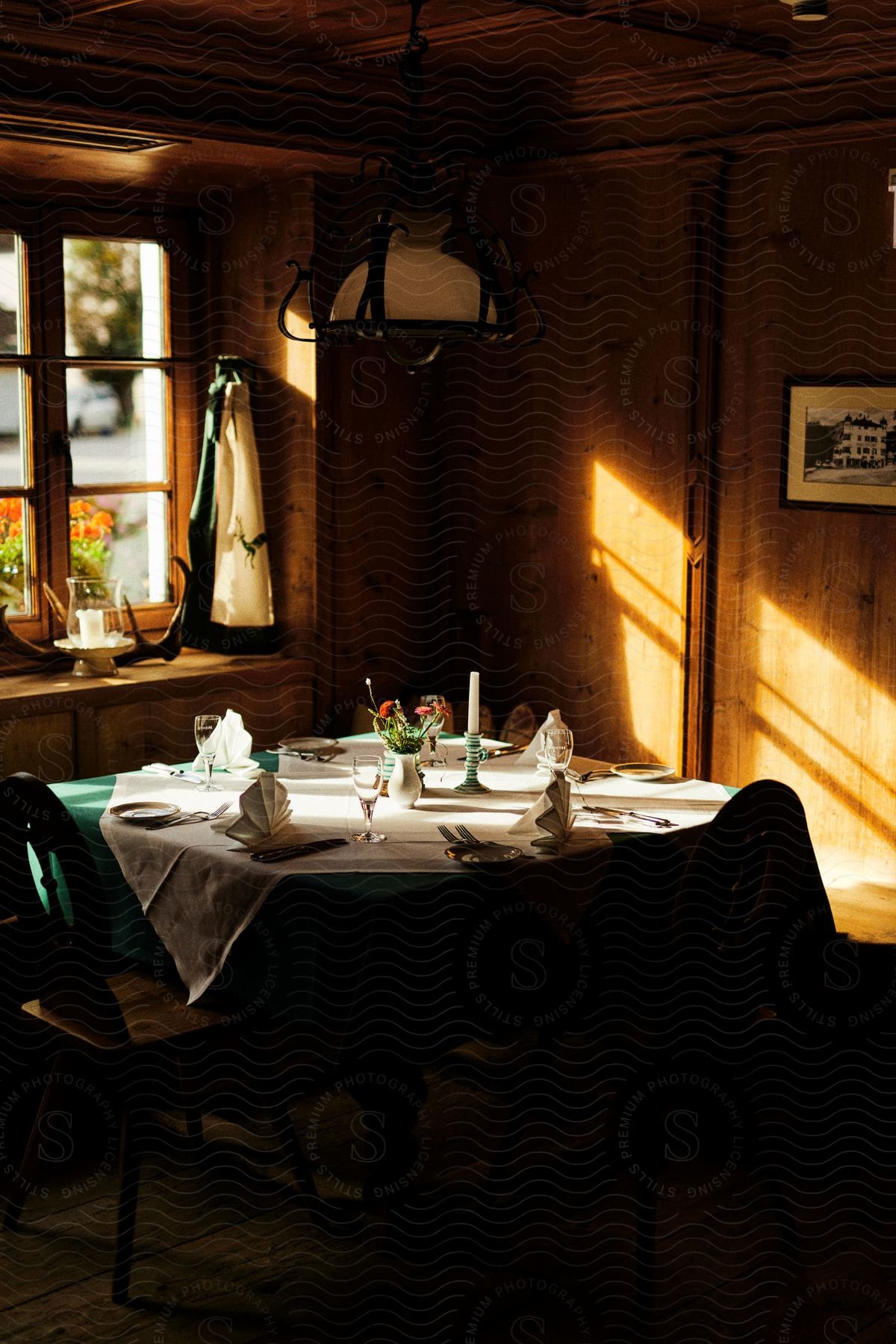 The interior of a wooden house where there is a table with chairs and the table is set with cutlery plates and glasses and there is a window where sunlight is passing through