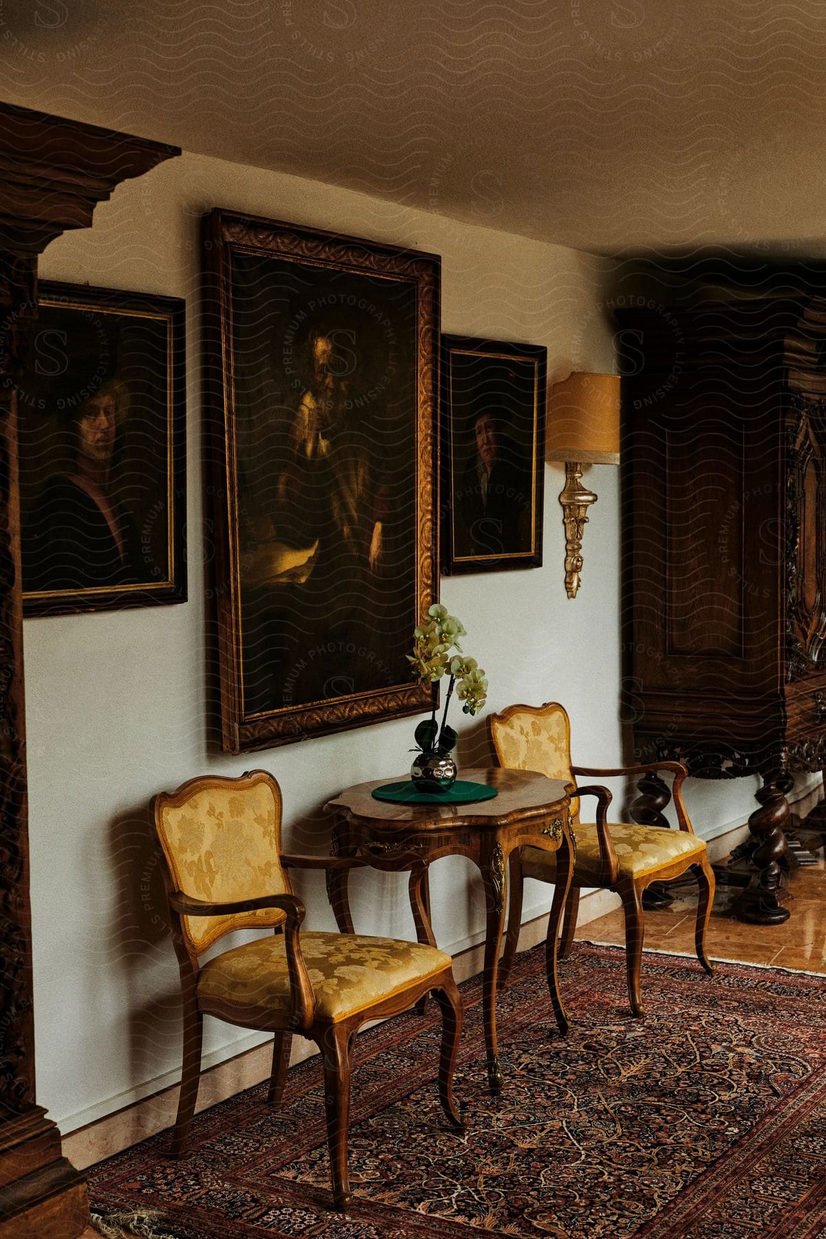 Two older chairs are situated against a wall with three portraits.