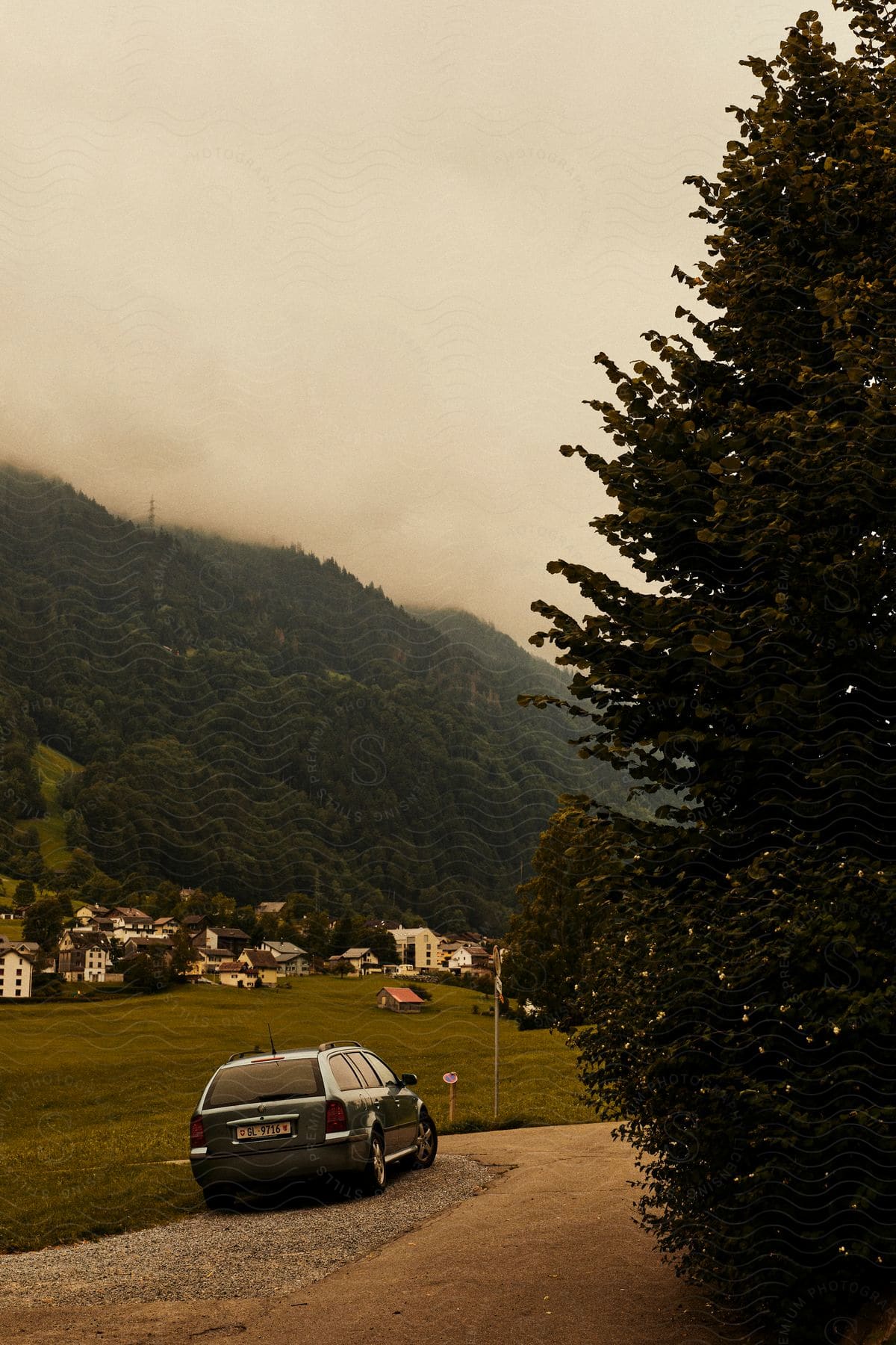 Panorama of a vehicle parked next to a pasture field with rural houses during the day with cloudy sky