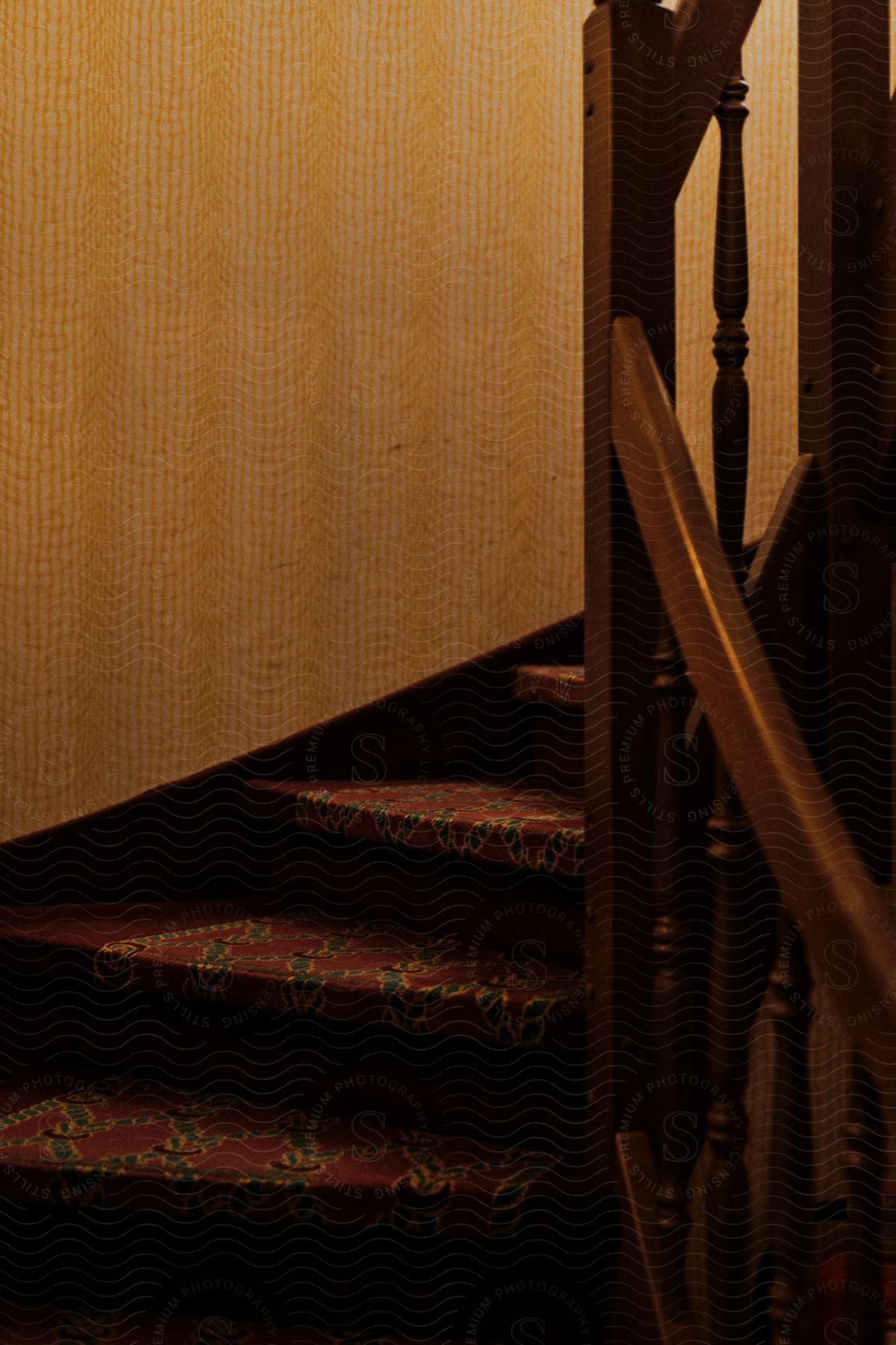 Interior curved staircase with blue rope design on red carpeted stairs, yellow wall papered wall and wood banister inside railing.