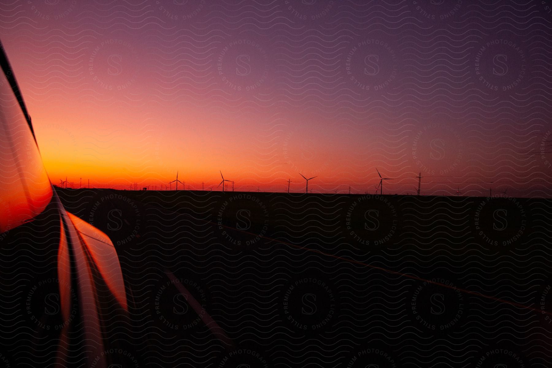 Wind turbines stand in the distance under a red sunset sky