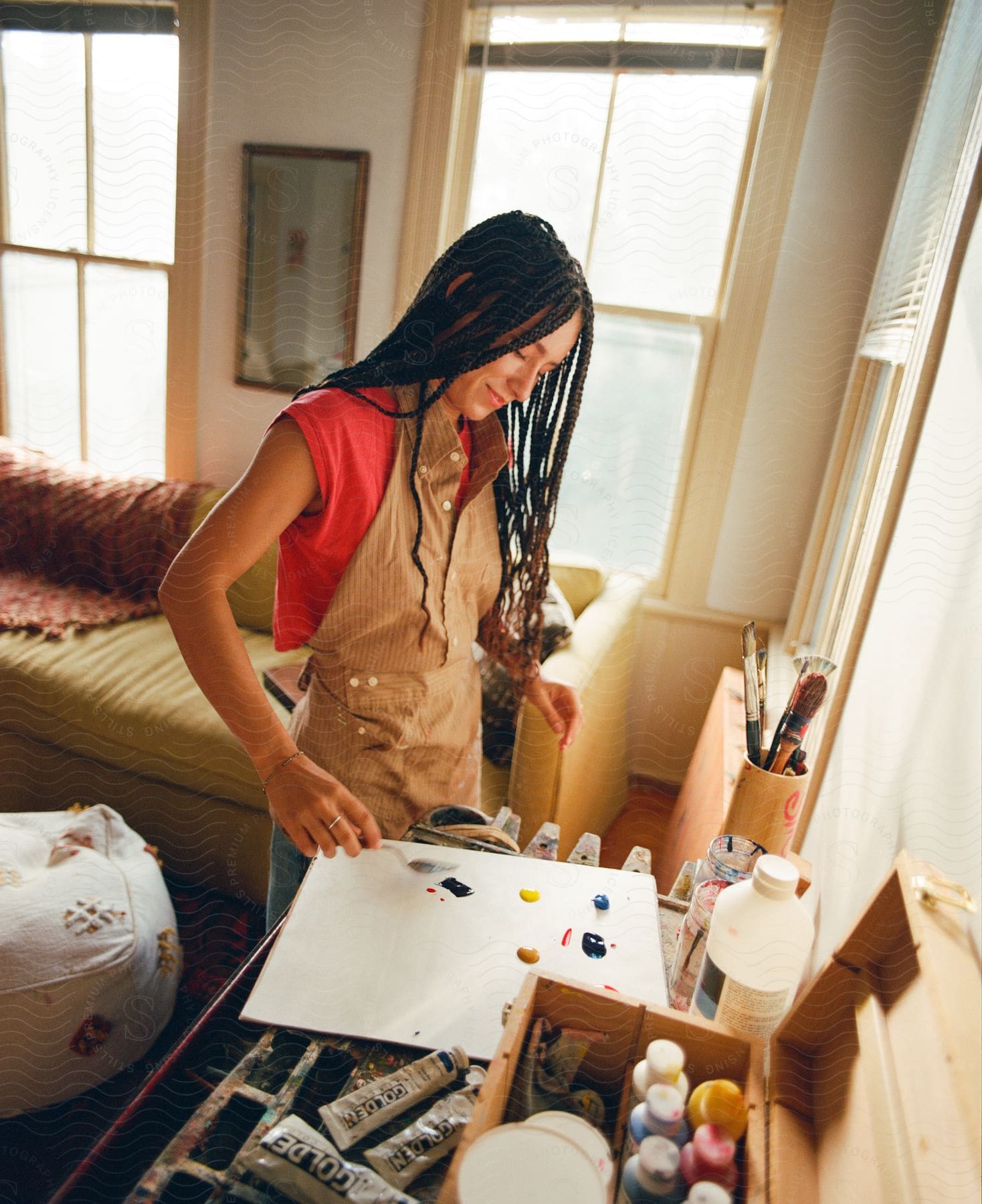 A woman stands in her living room working with tubes of paint