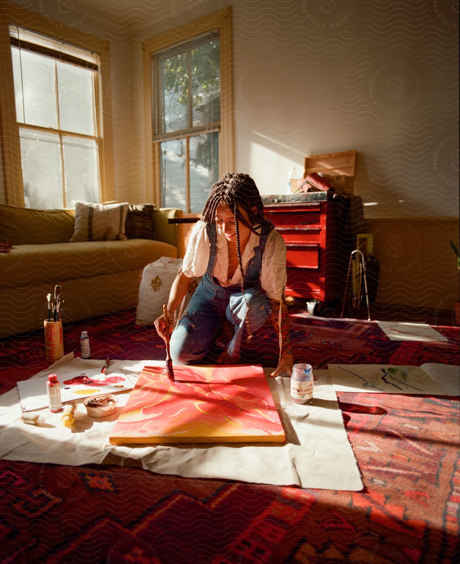 An artist immersed in her work, painting on a canvas on the floor in a room bathed with sunlight.