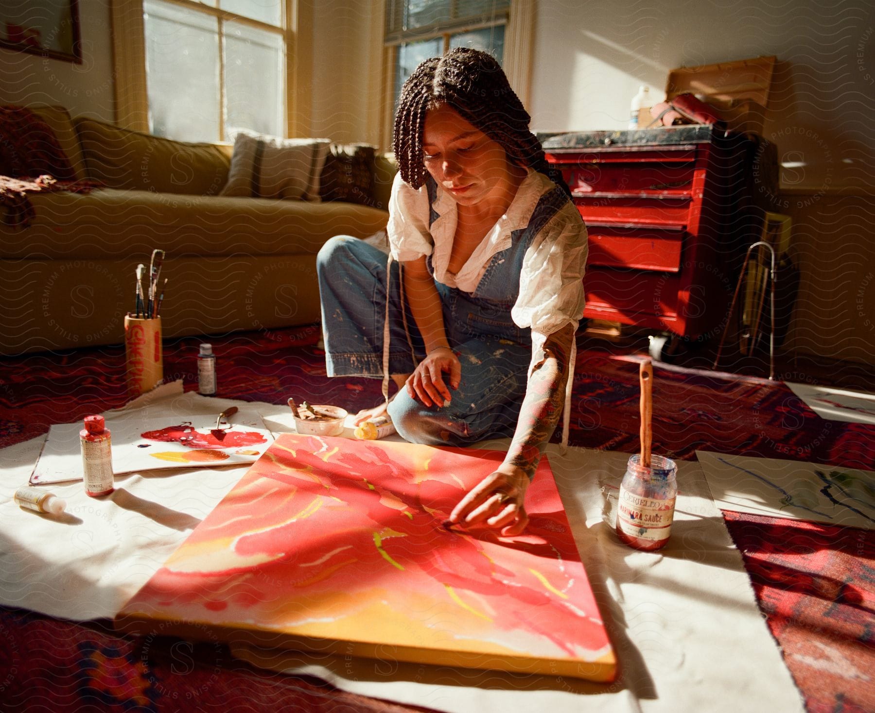 A woman squatting down painting a picture with red paint inside a room