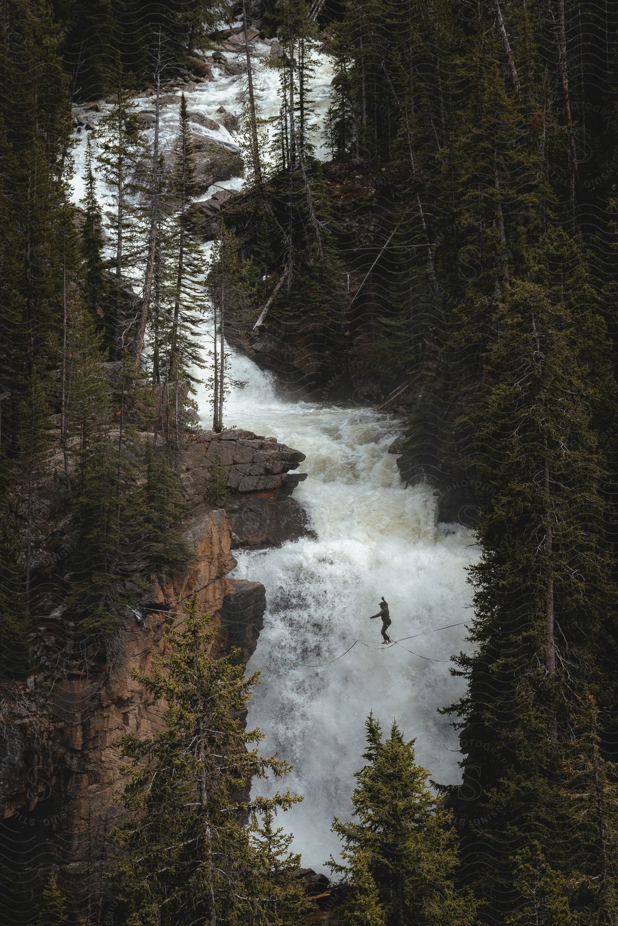 a person walking on a sling bridge across the mountain with a stream flowing by