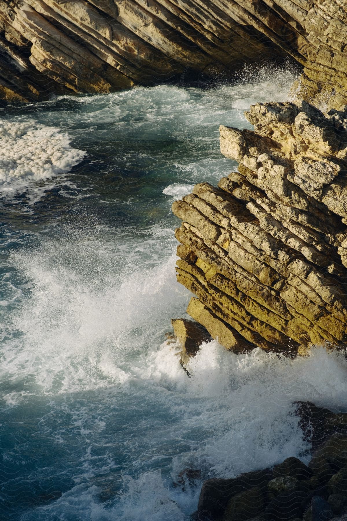 Waves crashing against stratified rocks on the coastline.