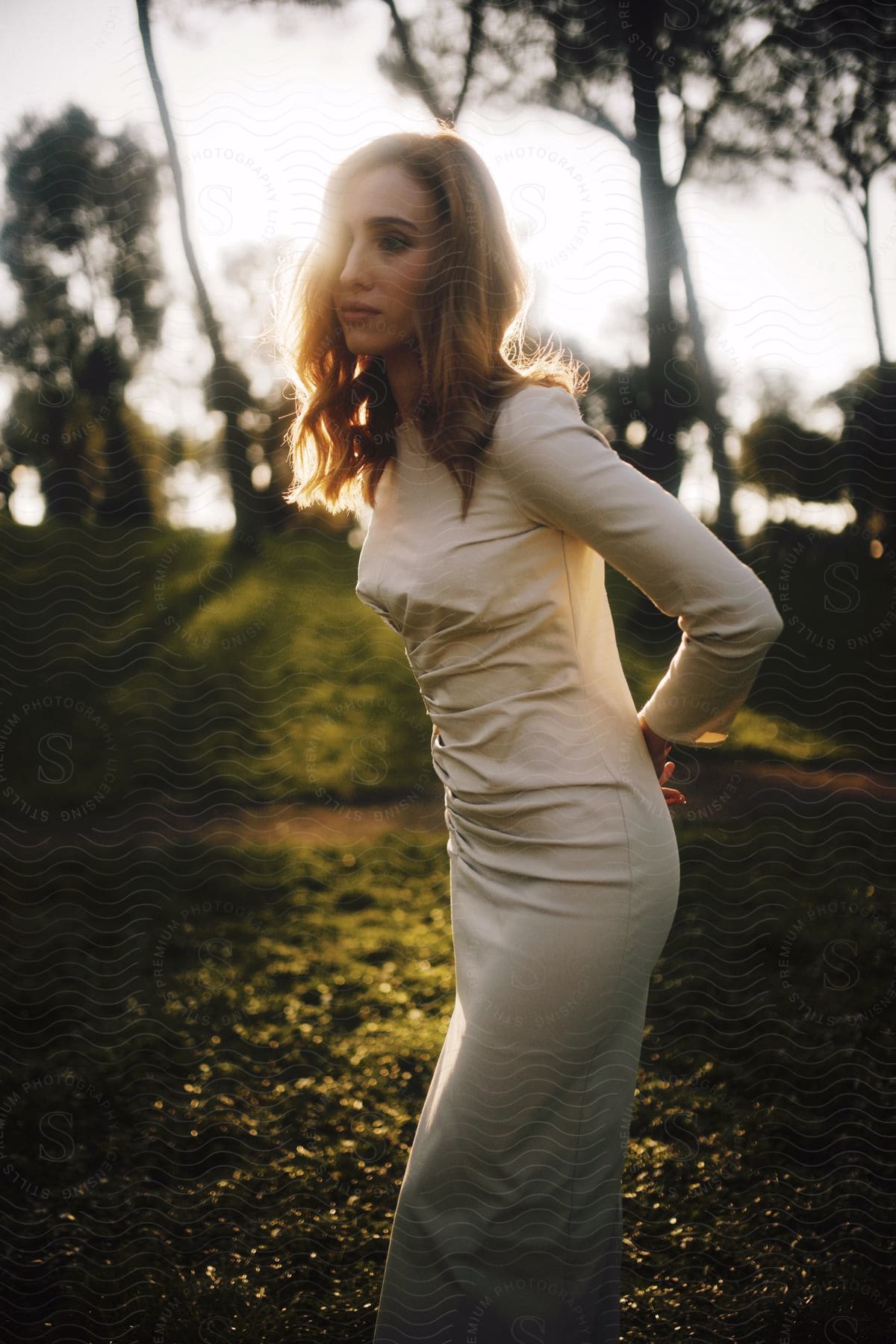 Woman in a white dress posing in a forest at sunset.
