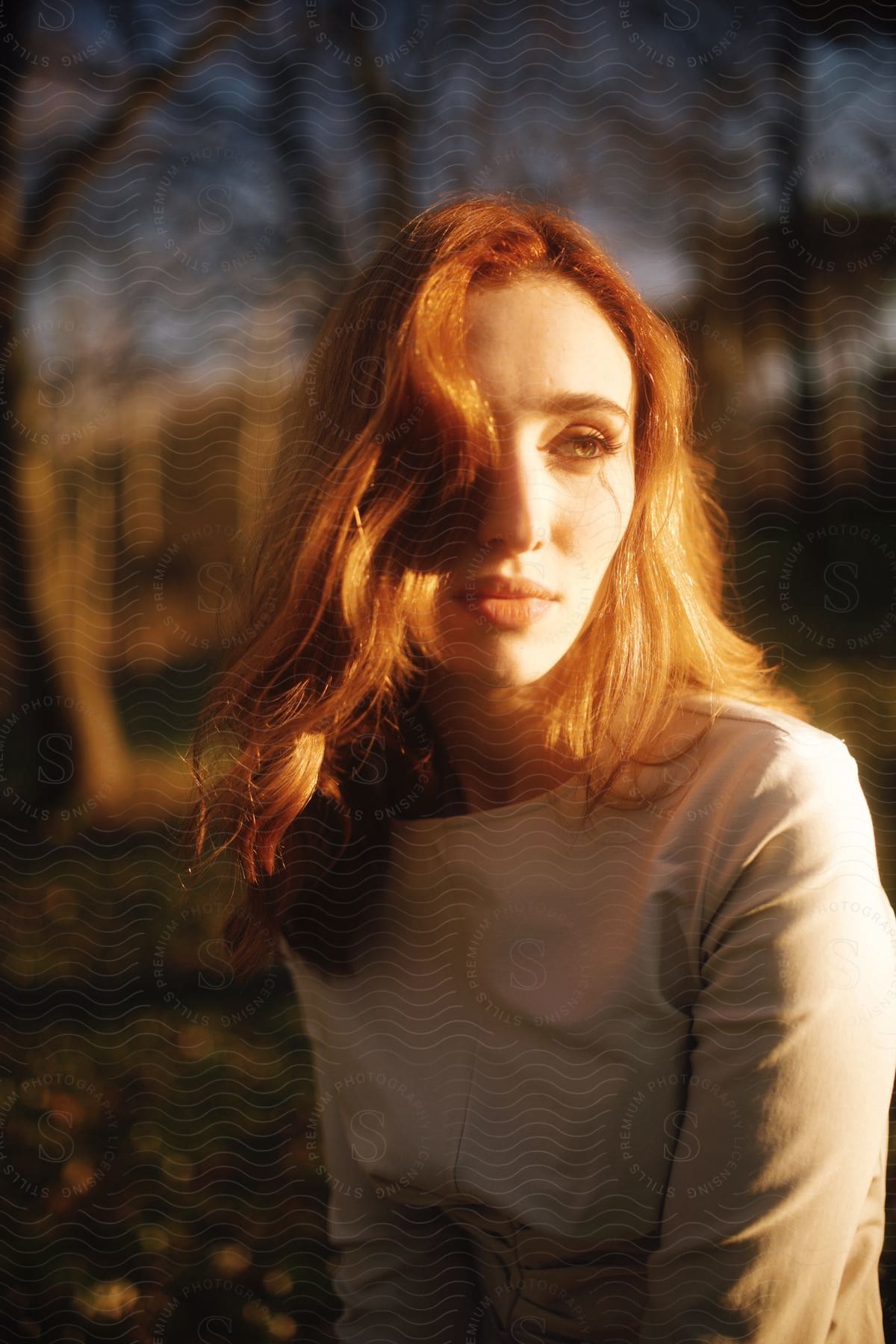 Sunlight shines onto face of redheaded woman wearing fashionable attire outdoors.