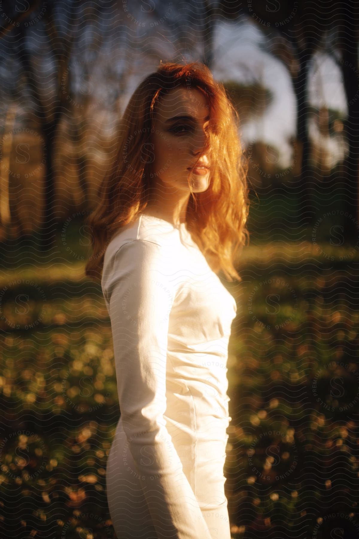Redheaded model wearing fashionable dress stands in field.