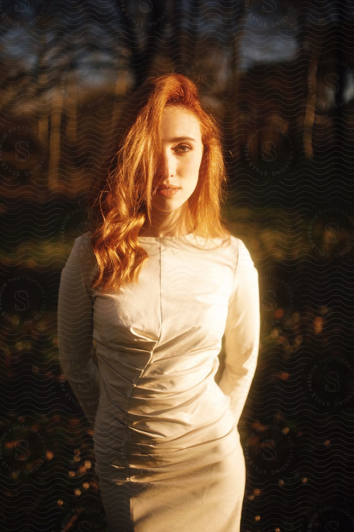 A women is wearing a white dress outside with the setting sun shining on her.