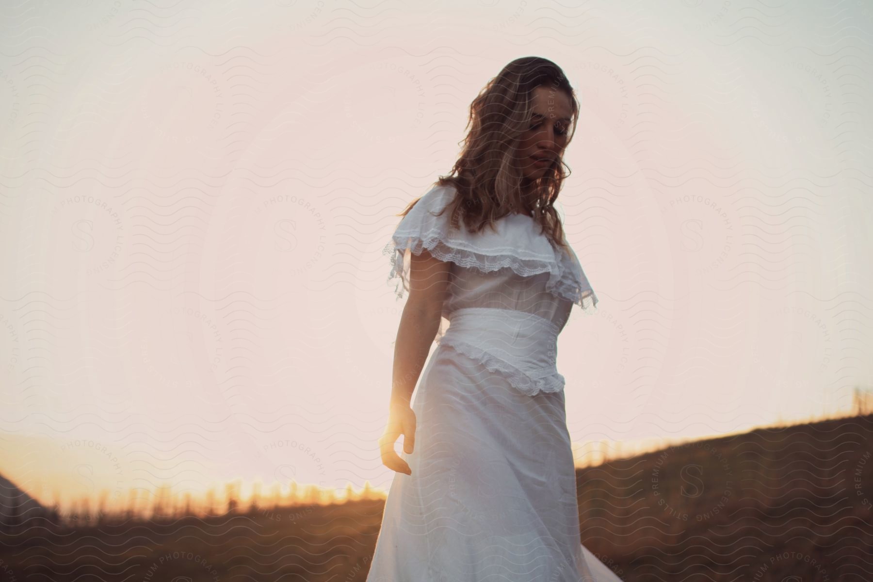 Woman in a white dress with sunlight behind her in a field at dusk.