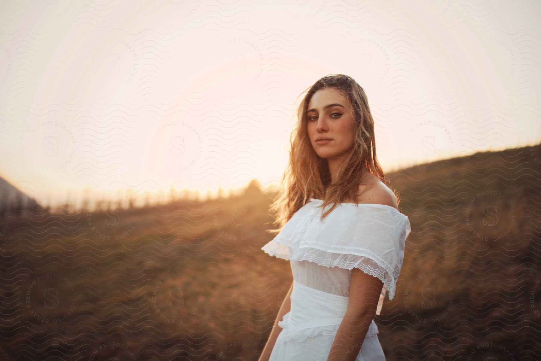 A woman standing on a grassy hill in a white dress