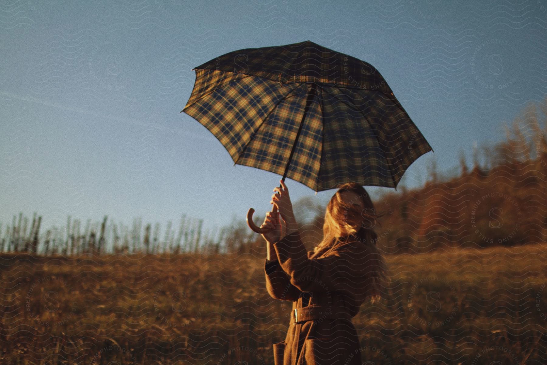 The sun shines upon a woman standing in a rural field holding an umbrella