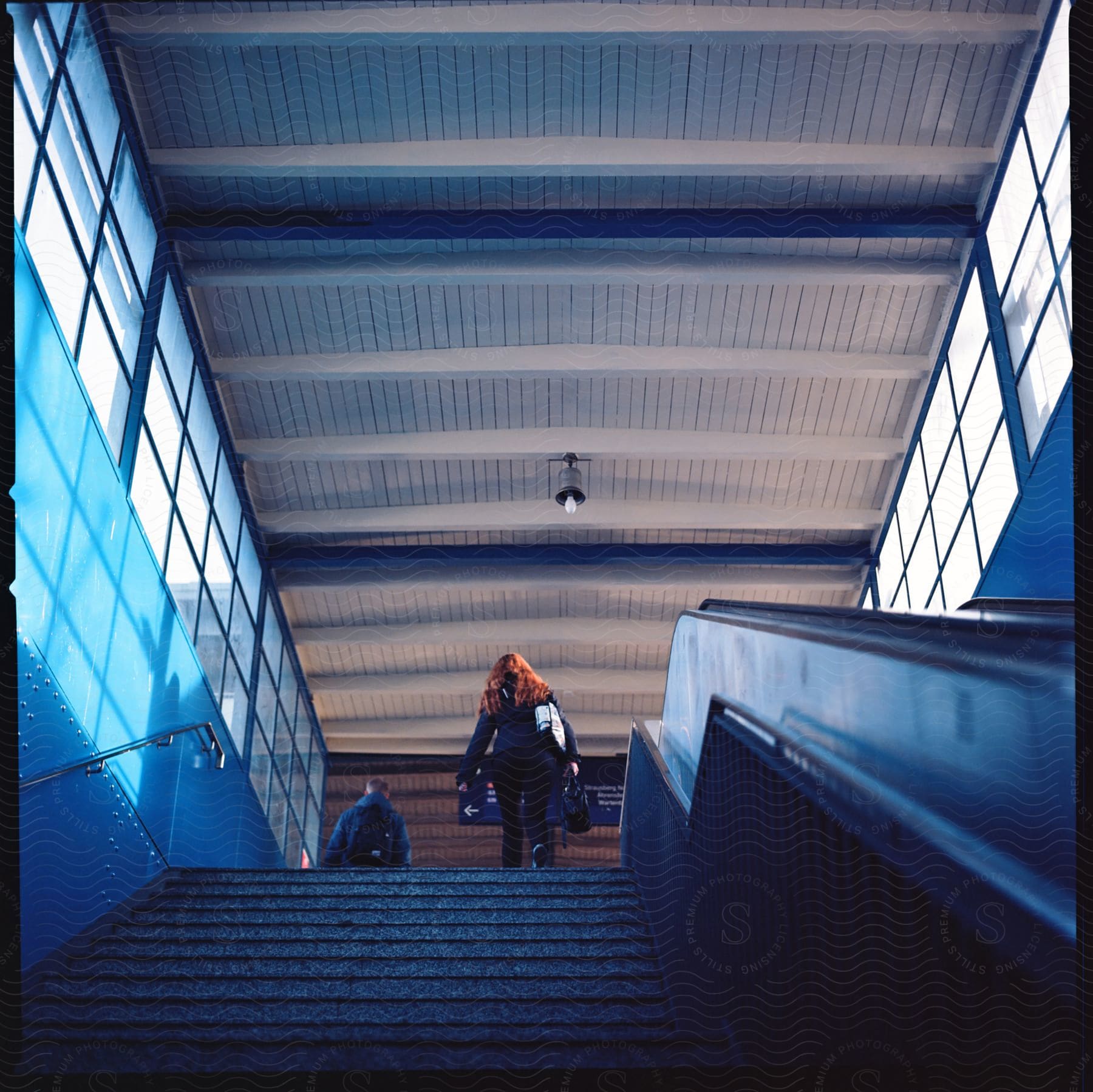 A woman walks to the top of the stairs at a terminal as a man walks ahead of her