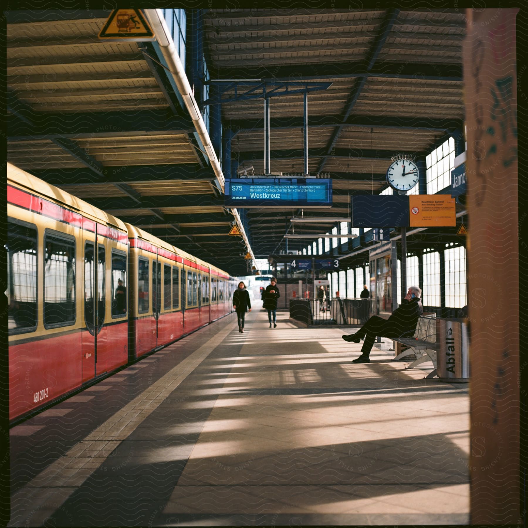 A man sits on a bench in the subway station as two people walk near the train