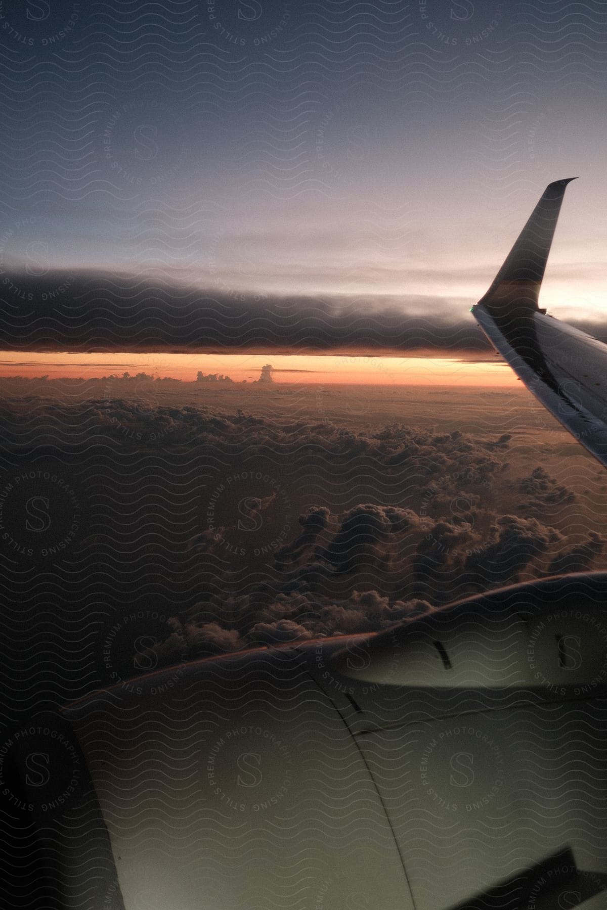 A photo from inside an airplane showing the wing and engine, with the sun setting over clouds and the sky.