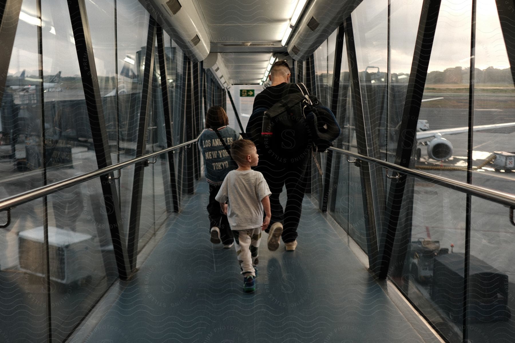 A father walks along an enclosed bridge at an airport towards a stationary airplane.