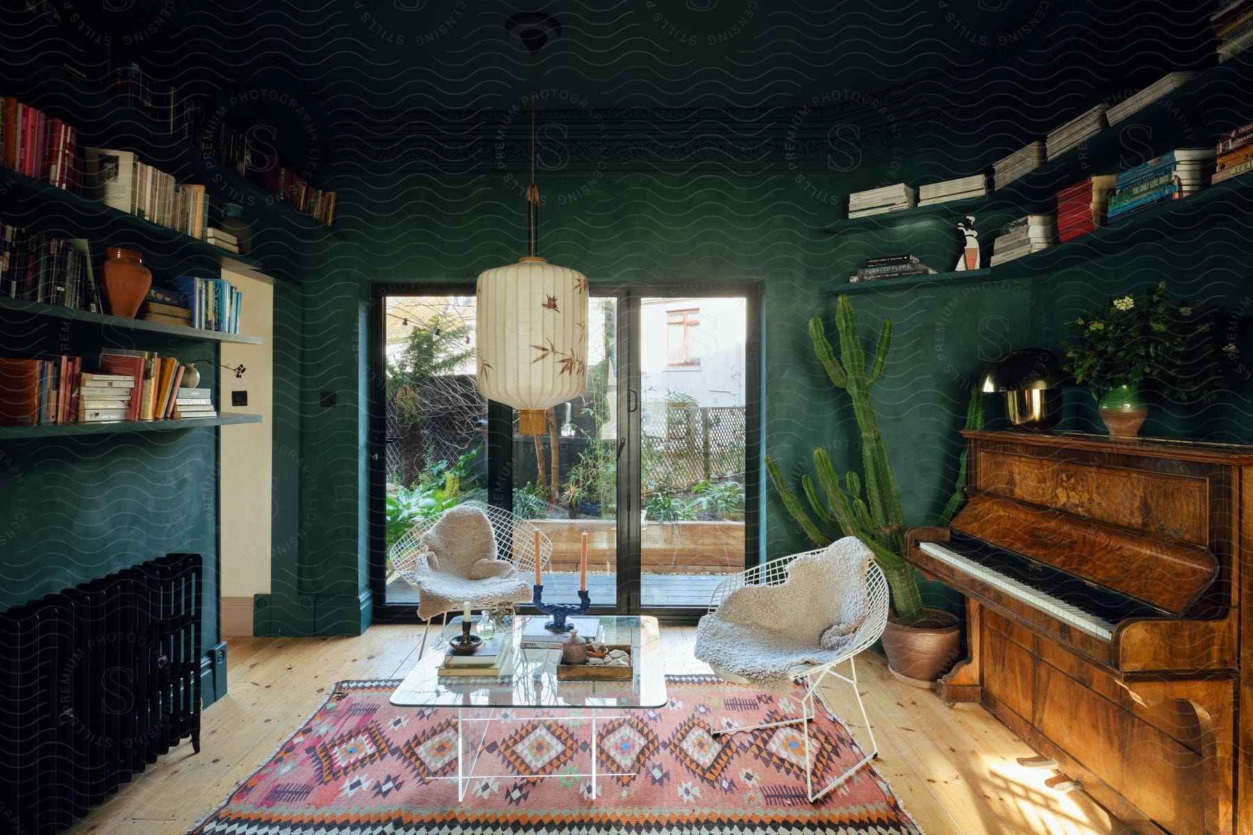 Living room near patio windows with a glass table and chairs in the middle and a piano near a catus and books on shelves on the wall