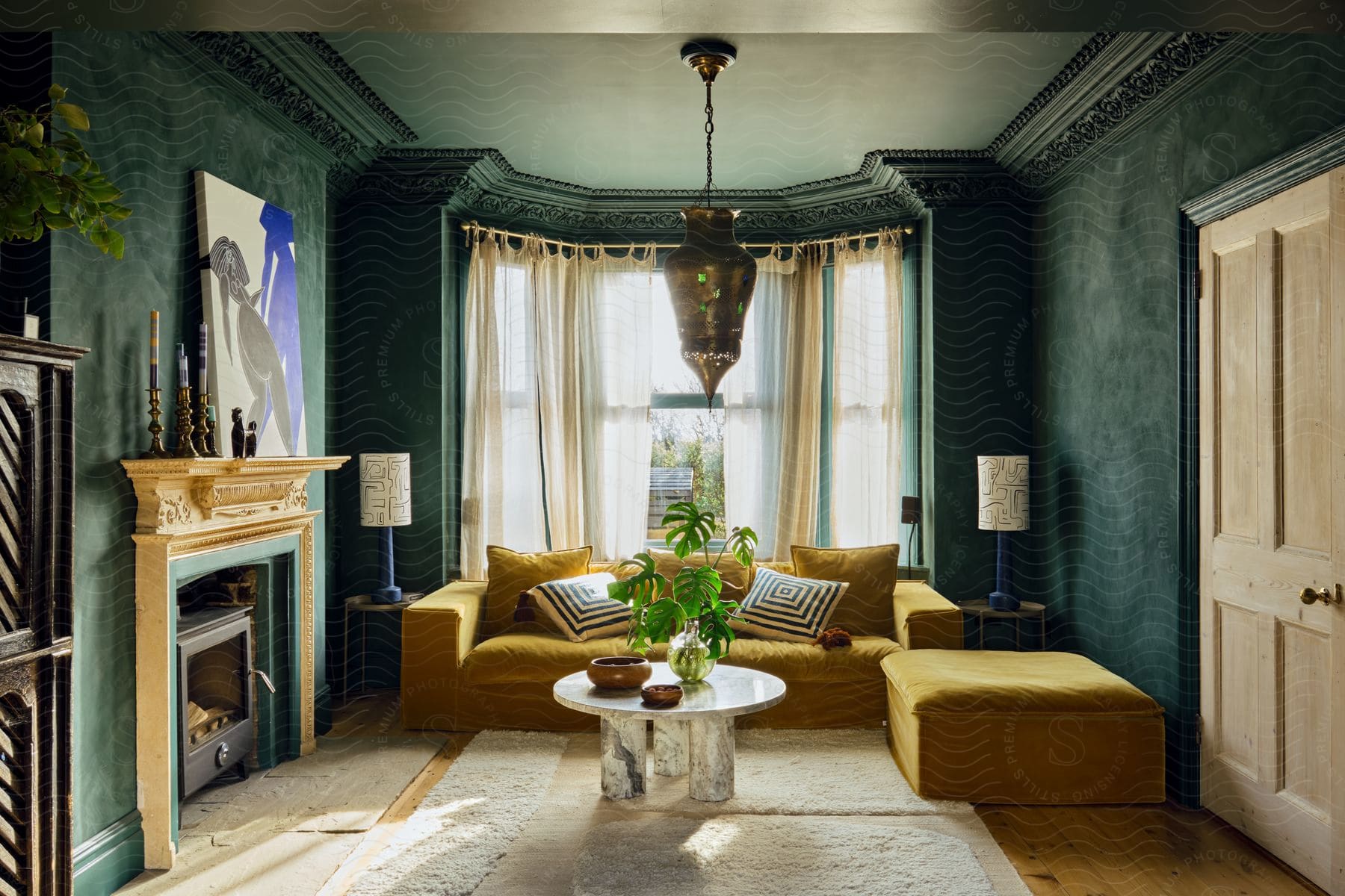 Living room with a fireplace under the mantle and houseplants on the round table in front of the couch and sheer curtains on the bay windows