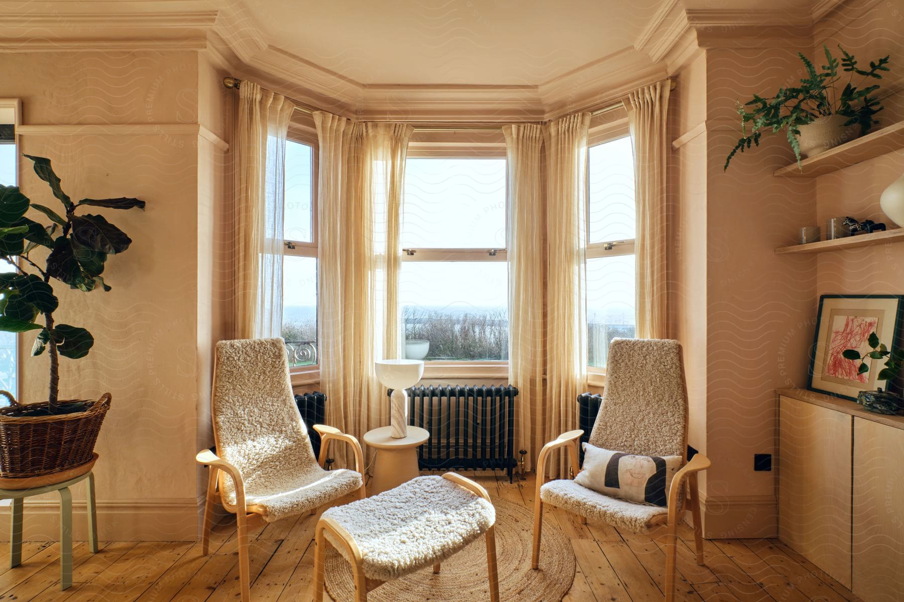 Bright bay window seating with two textured chairs, round table, and indoor plants, in a room with wooden floors.