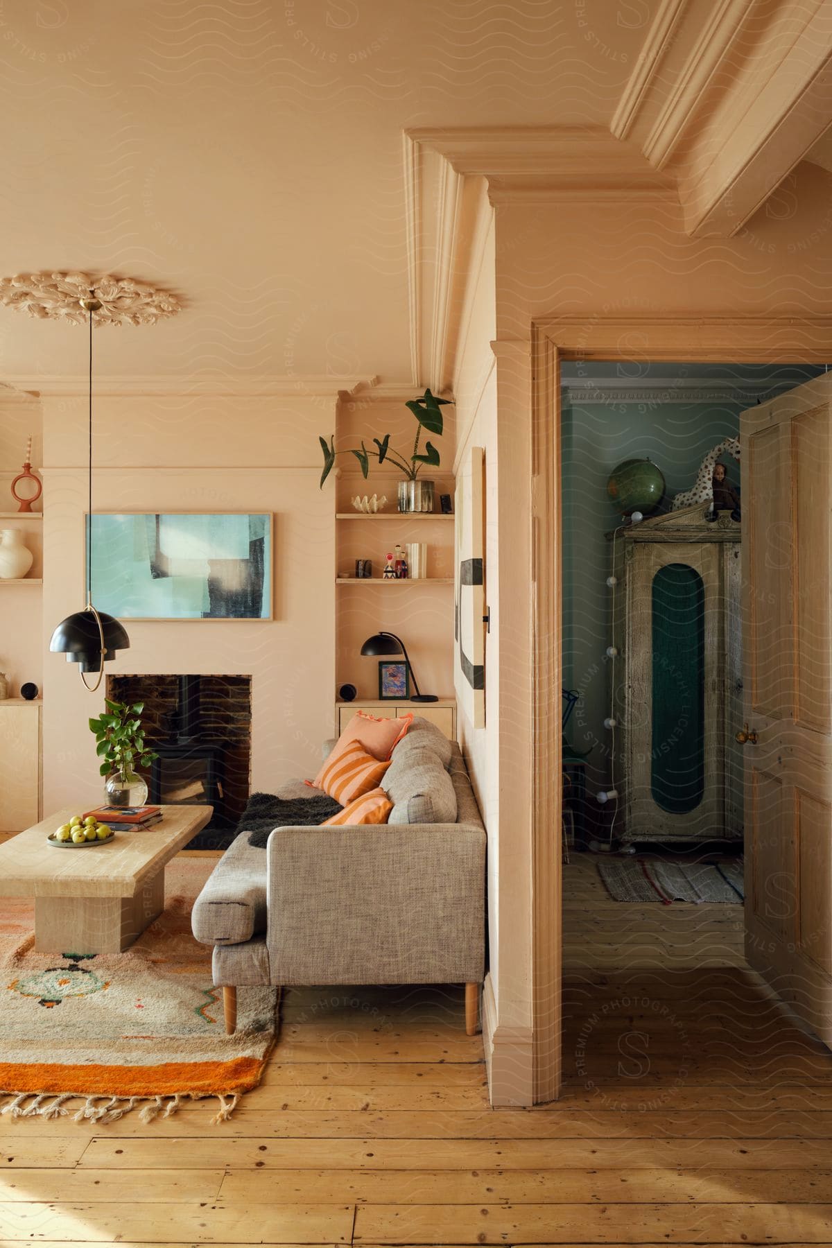 Living room with sofa, fireplace, and wall shelves, floral chandelier overhead, leading to room with antique wardrobe.