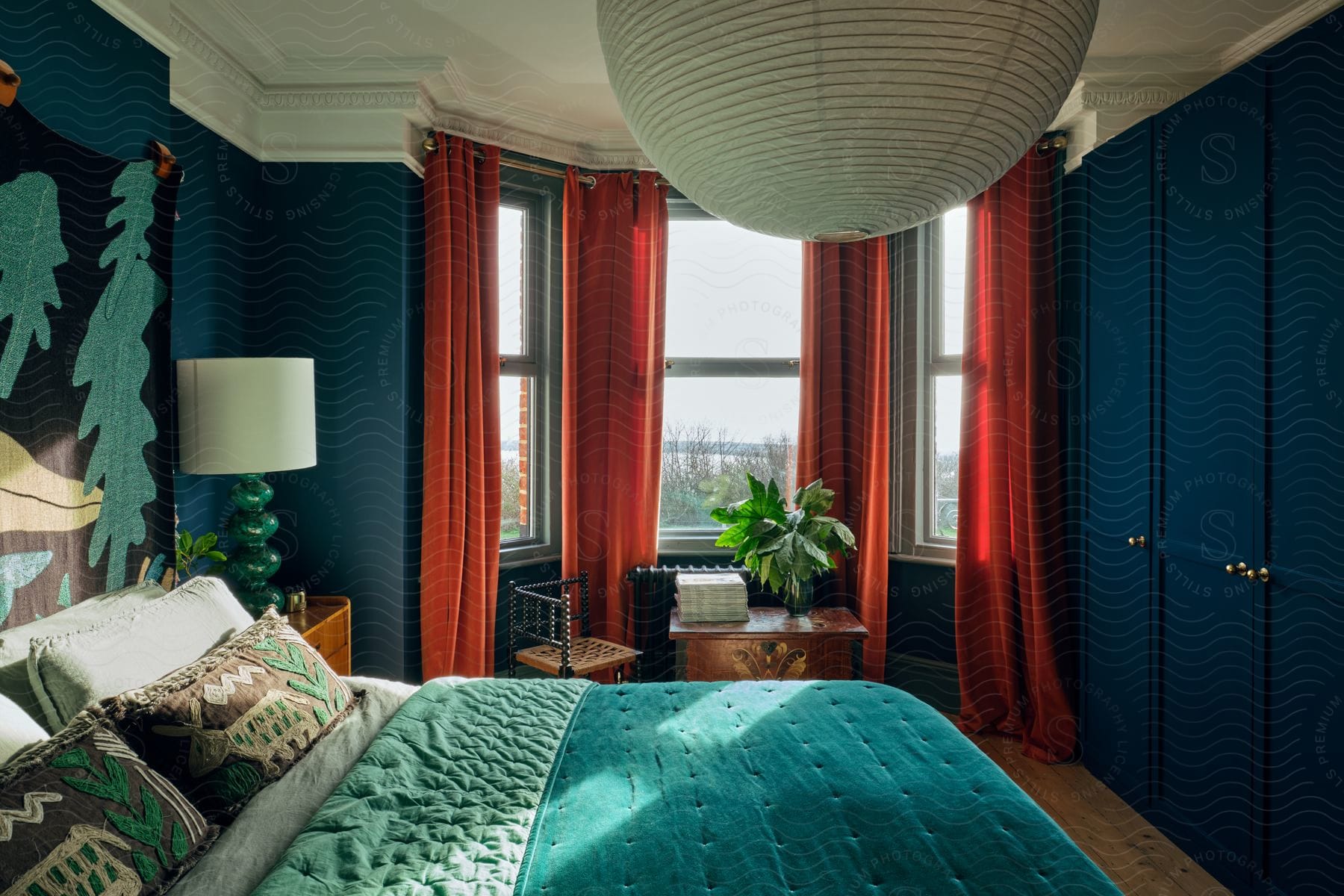 Bedroom with red curtains on bay windows open and a houseplant on the table