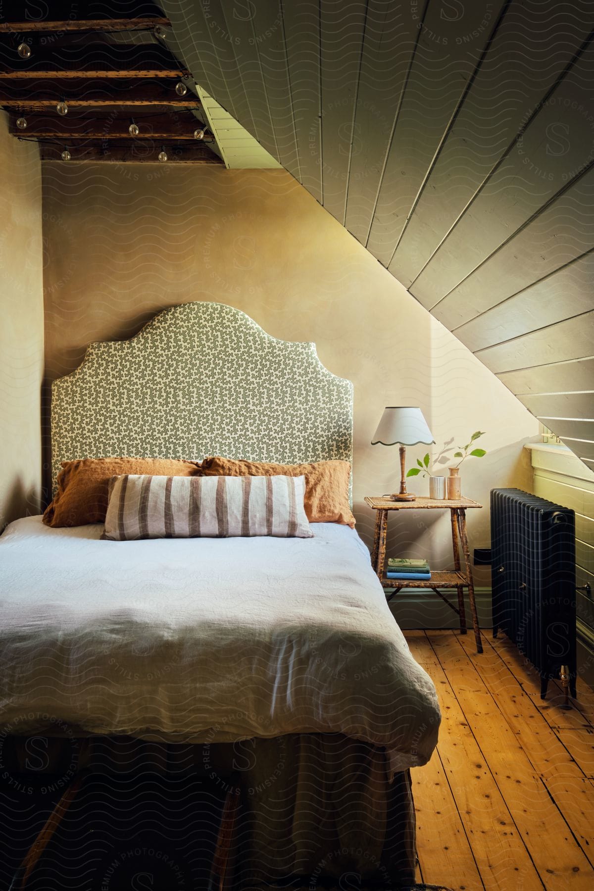 A bedroom with a slanted wooden plank ceiling hardwood floors and a tall fabric headboard