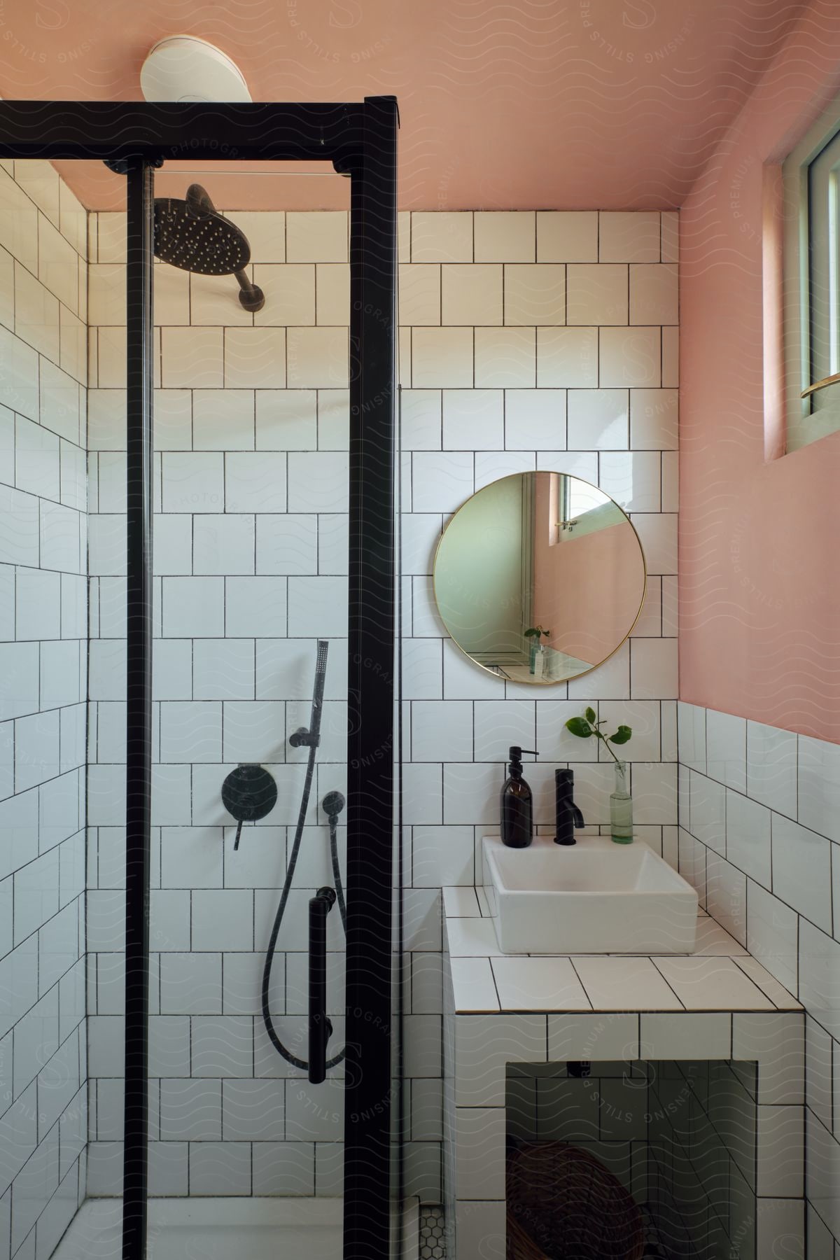 A modern bathroom features a sleek walk-in shower with black fixtures, white subway tiles, and a salmon-pink wall, complemented by a rectangular basin and round mirror.