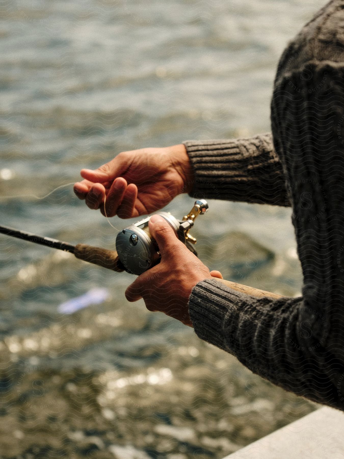 An adult is holding a fishing reel and pulling on fishing line over a body of water.