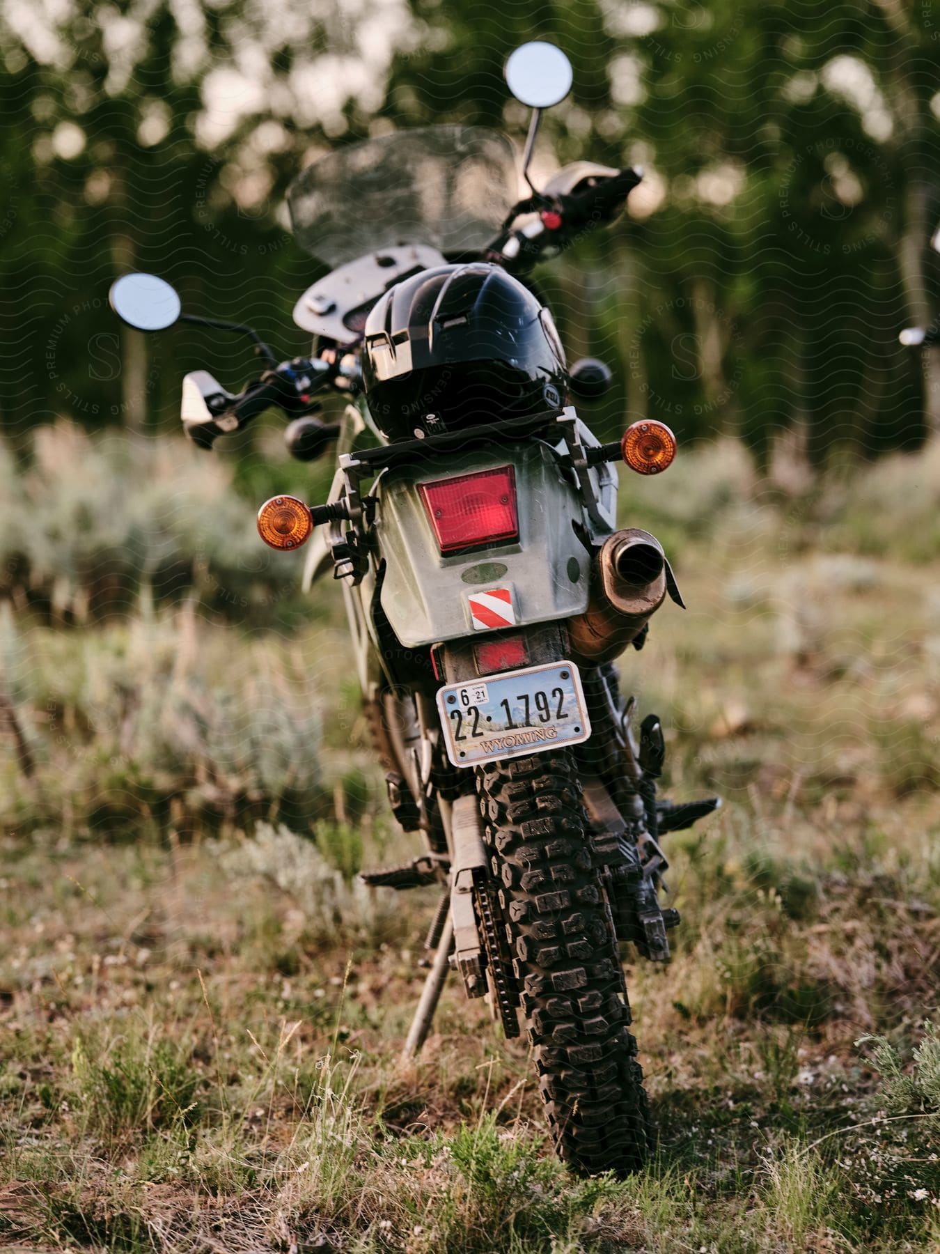 A black dirt bike with a Wyoming license plate, topped with a black helmet, parked in a field with trees in the background blurred.