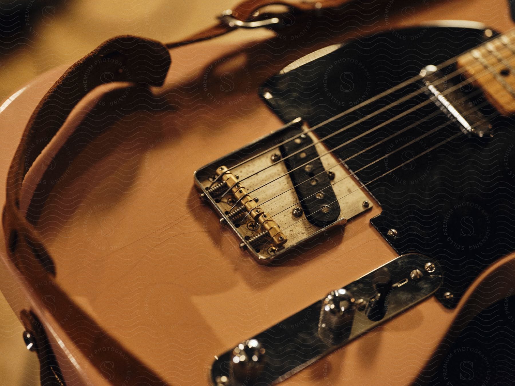 Stock photo of leather shoulder strap rests on pale colored guitar lying on a flat surface.