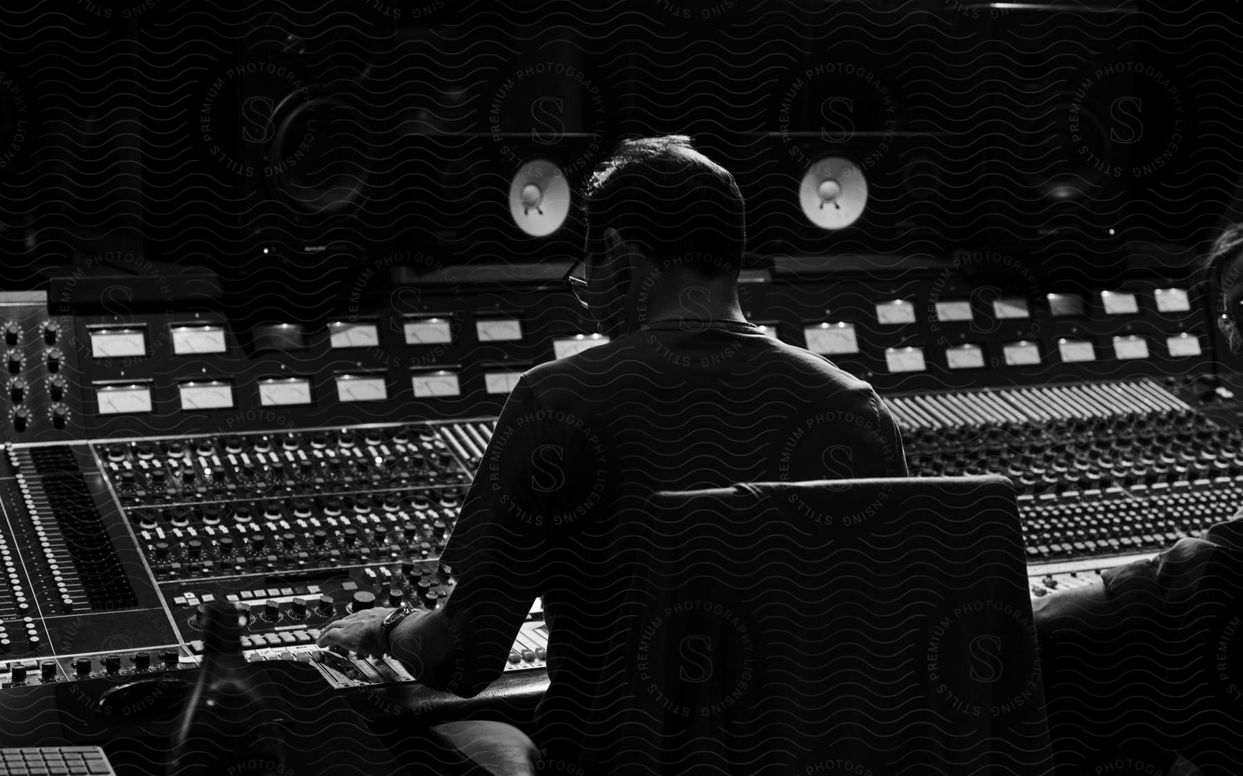 A man is sitting down and working on a large, electronic soundboard.
