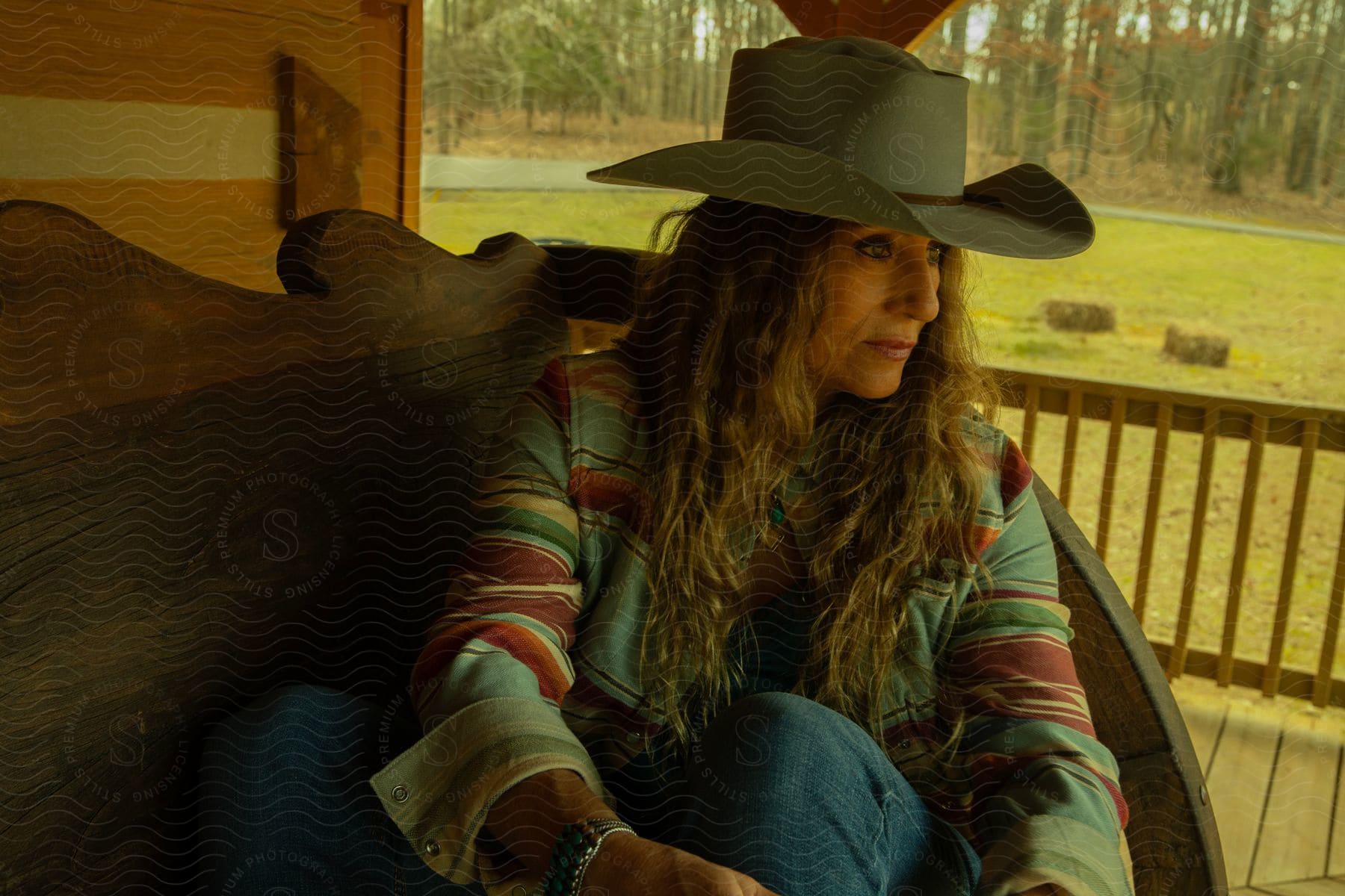 Woman wearing cowboy hat sits on bench on rustic porch.