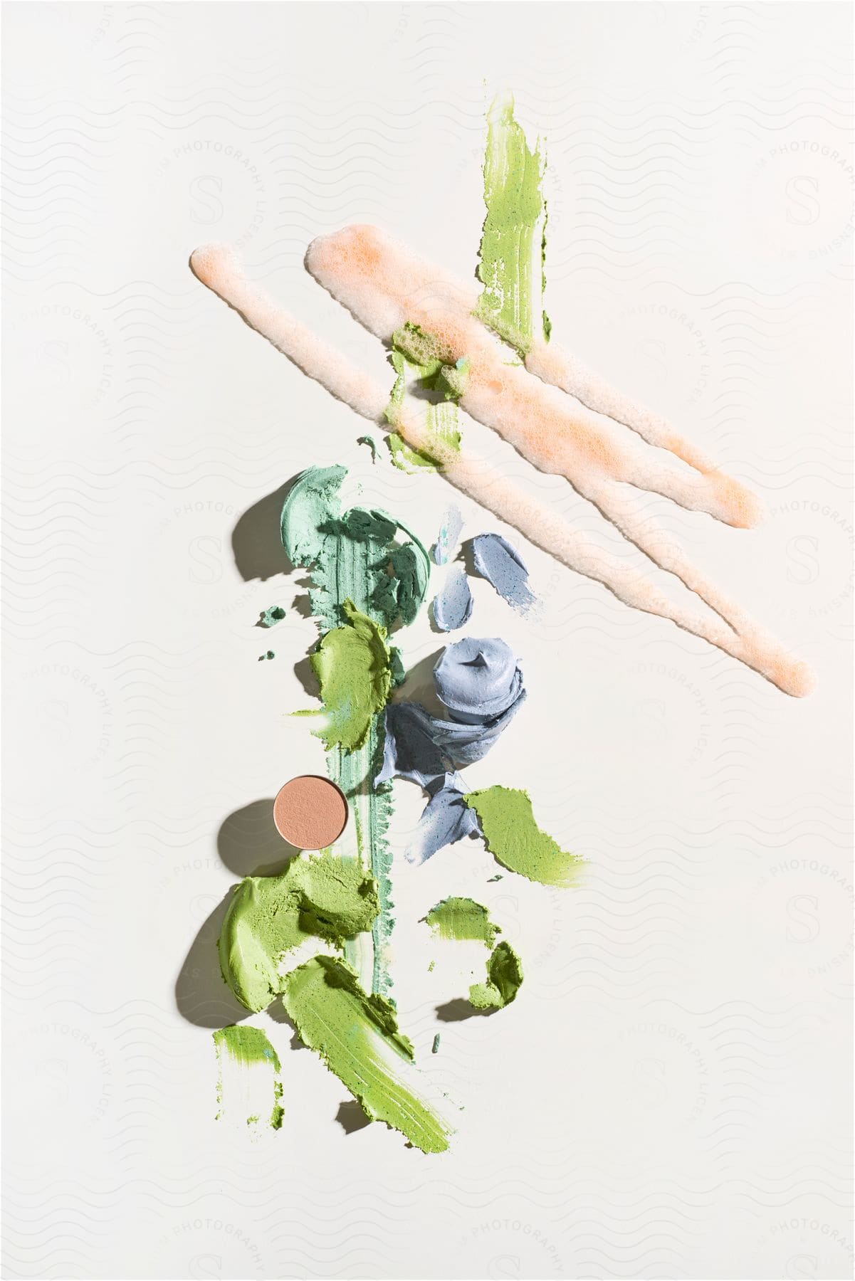 Artistic smears of green and blue makeup accompanied by cosmetic brushes on a clean background.