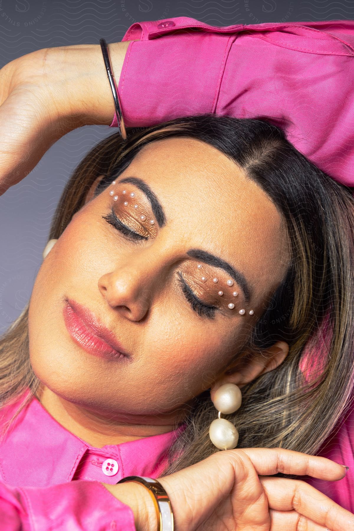 A woman in a pink shirt posing with eyes closed and pearls stuck to her eyelids.