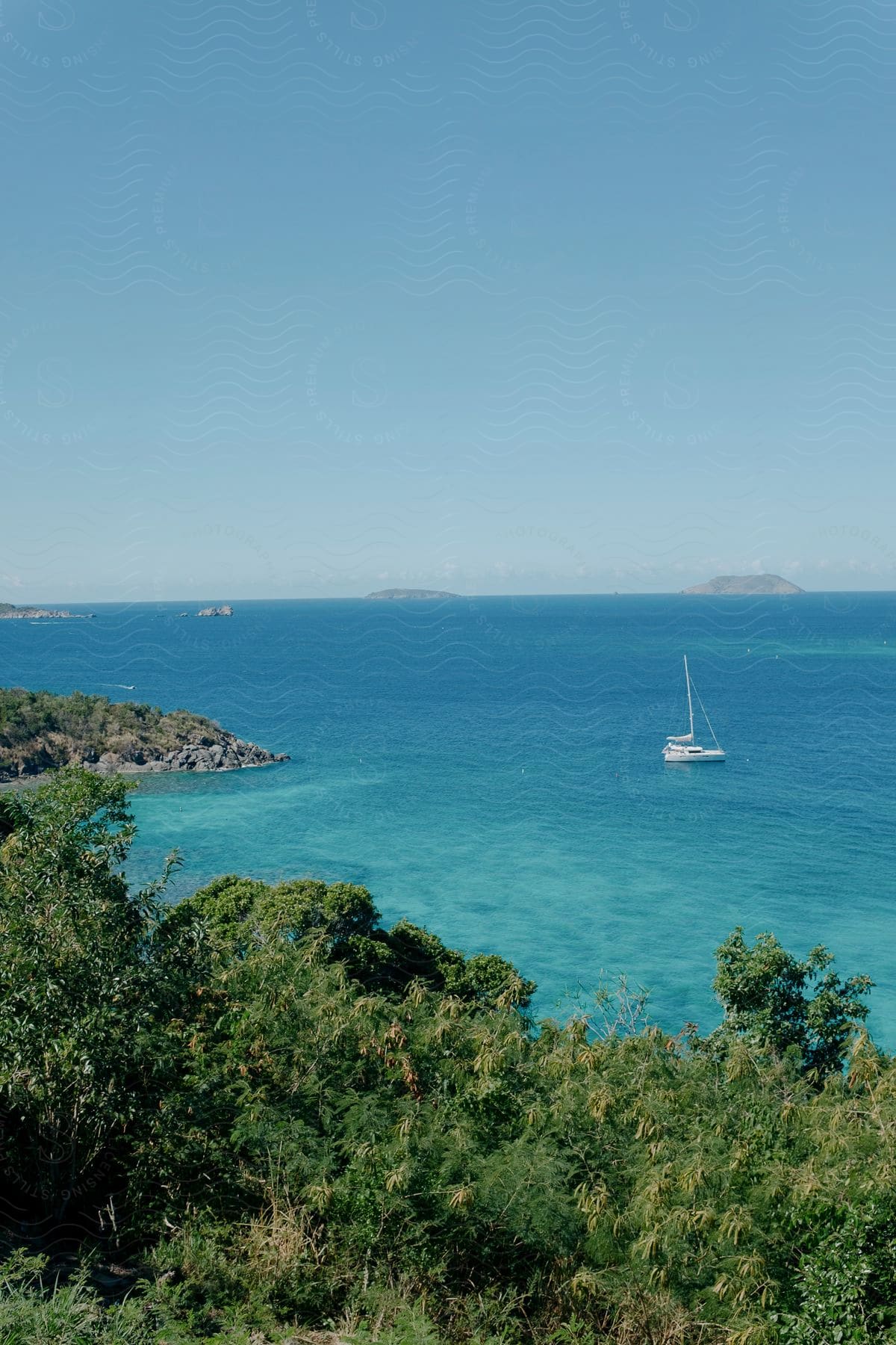 A white sailboat sits near a cove in bright blue ocean waters on a clear day.