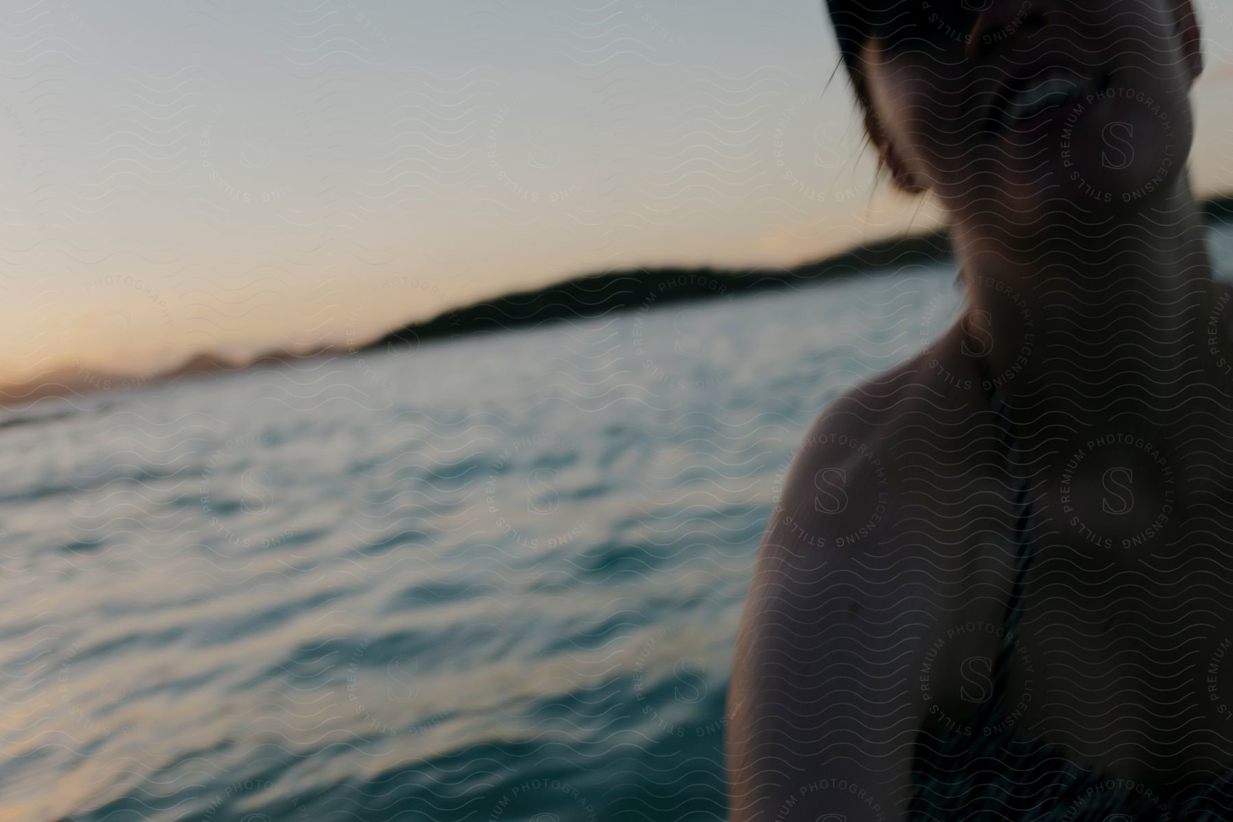 The image is a blurred capture of a smiling person near a body of water during dusk, creating a sense of movement and joy.