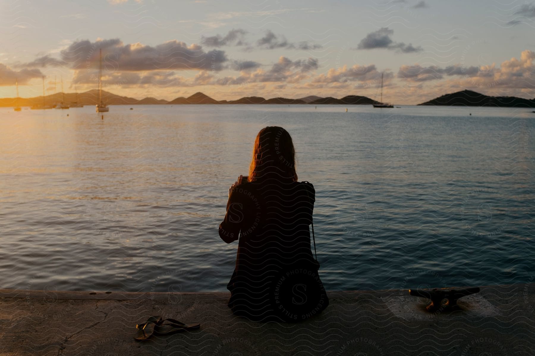 Landscape of a woman sitting on her back facing the sea with a sunset on the horizon