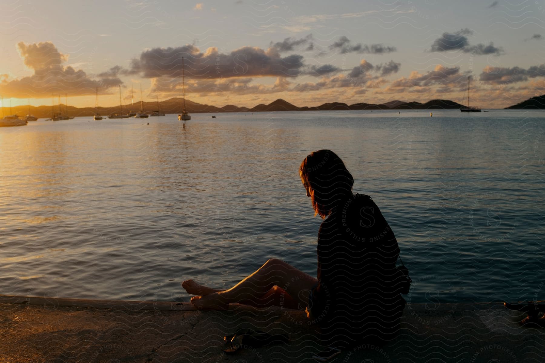 Woman sitting by the sea with a sunset on the horizon