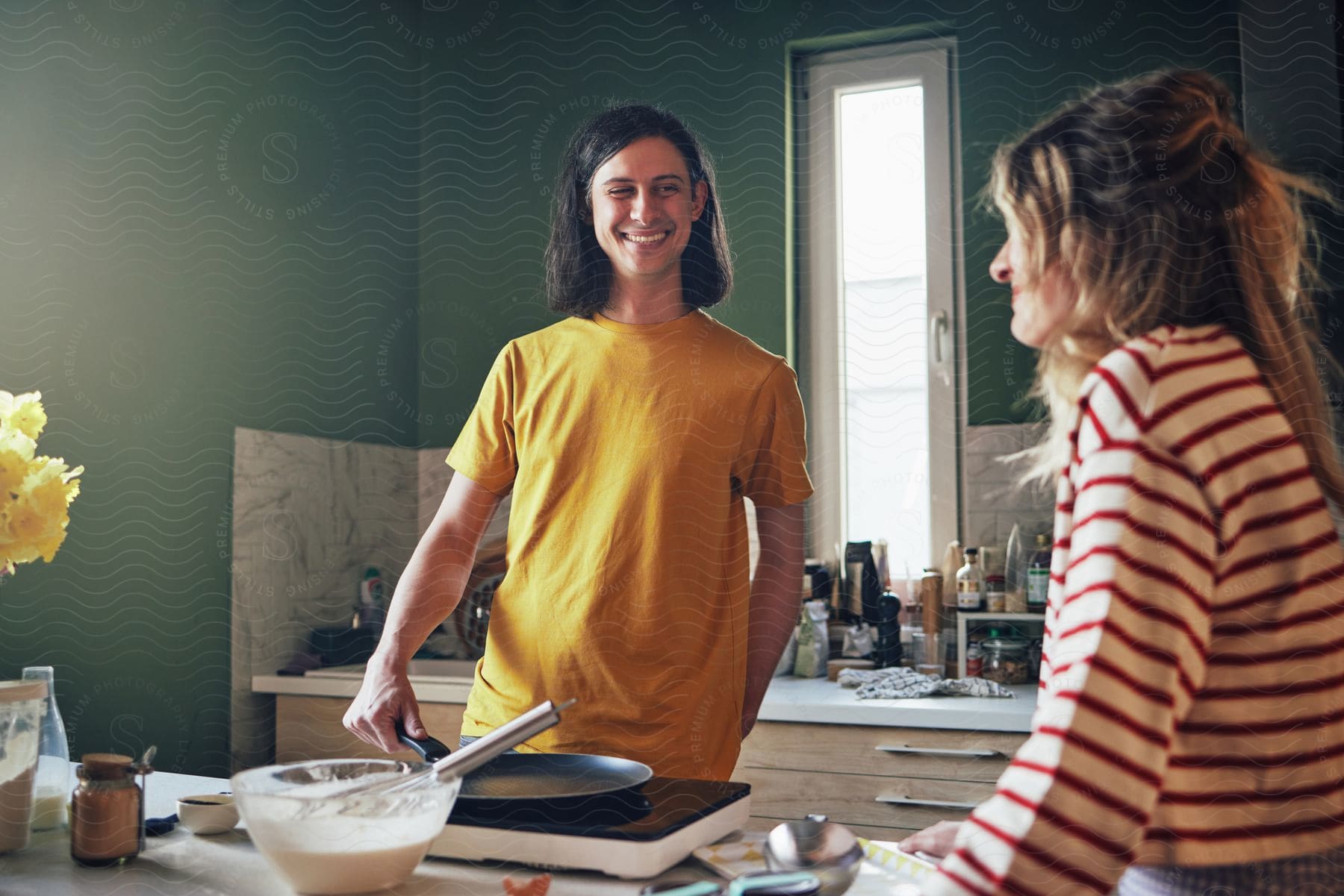 Two women stand in the kitchen over a frying pan and a mixing bowl