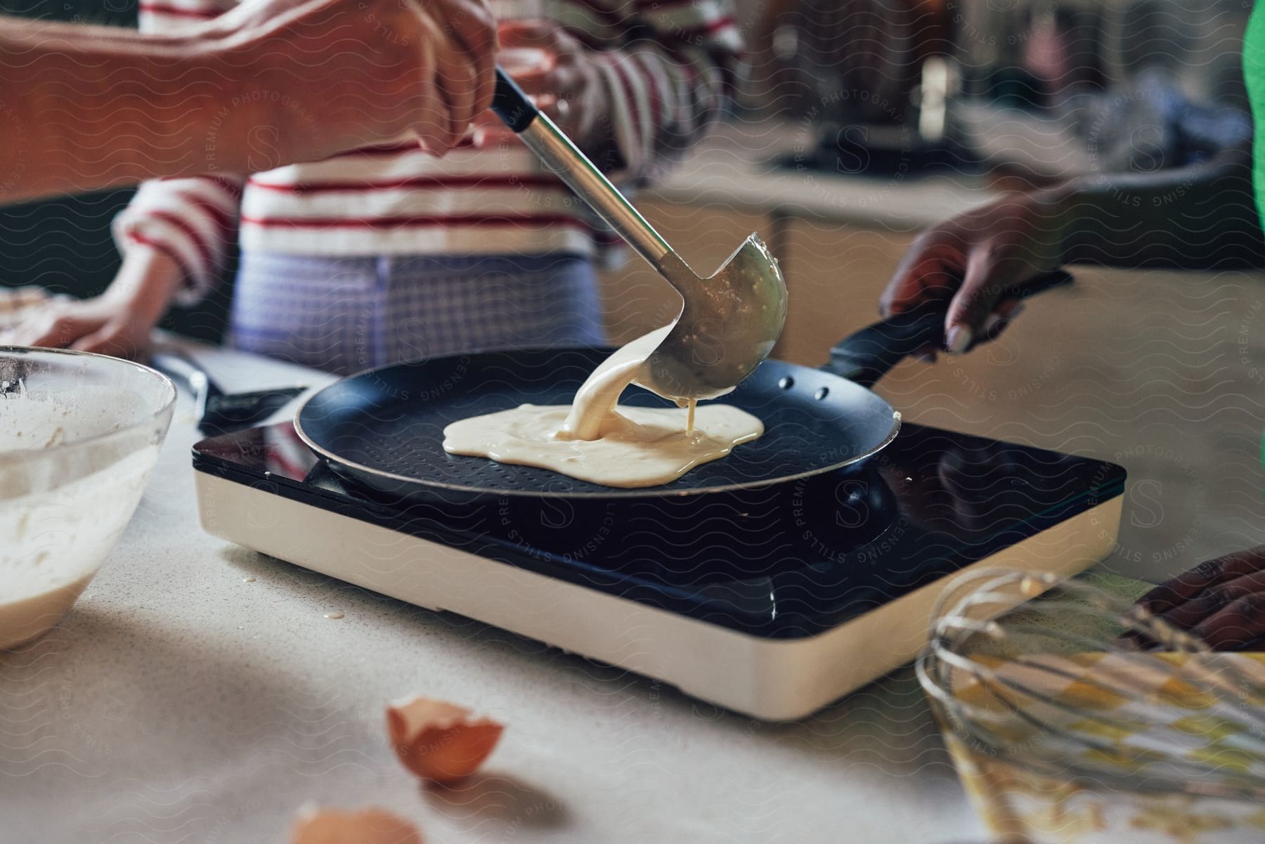 Stock photo of batter pours from a ladle as a person holds the frying pan