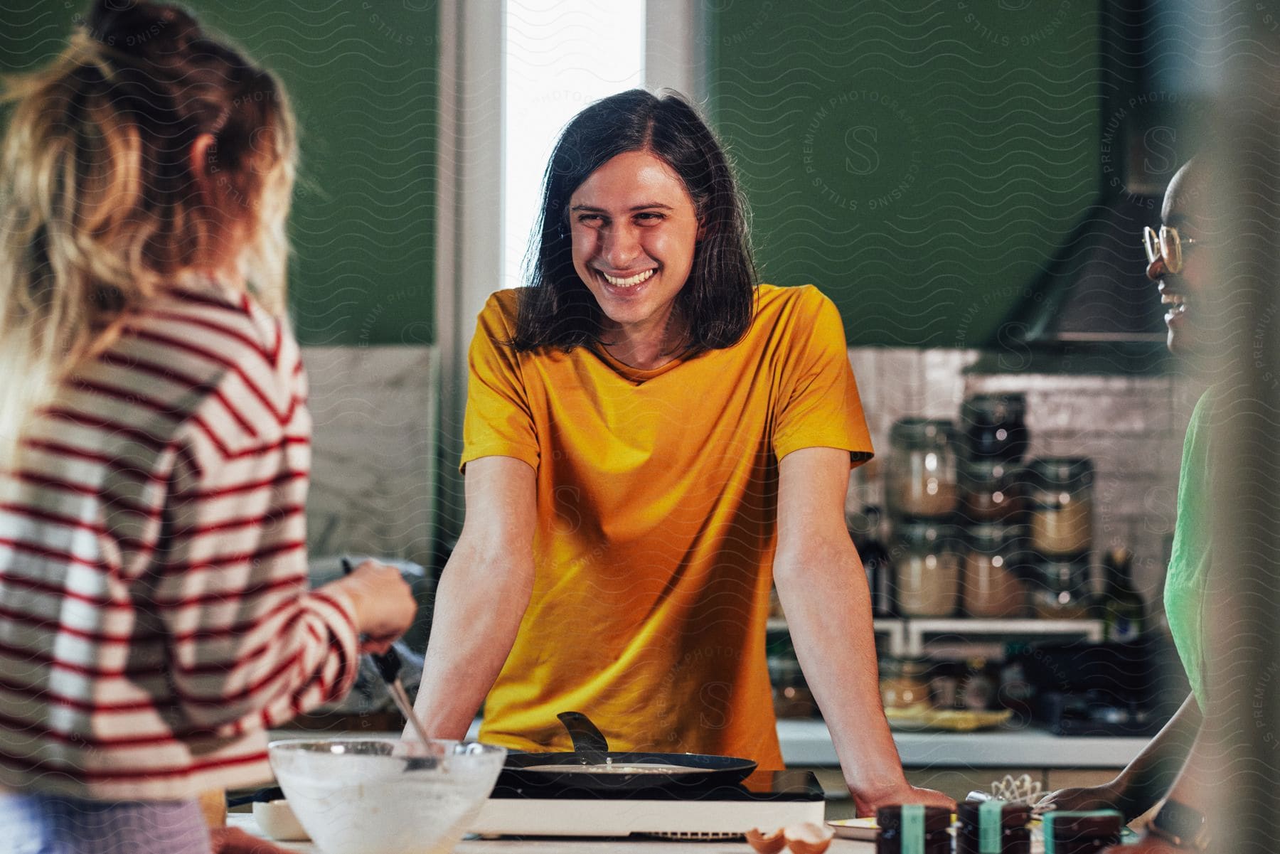 A young man with two female friends smiling broadly as he watches one make crepes